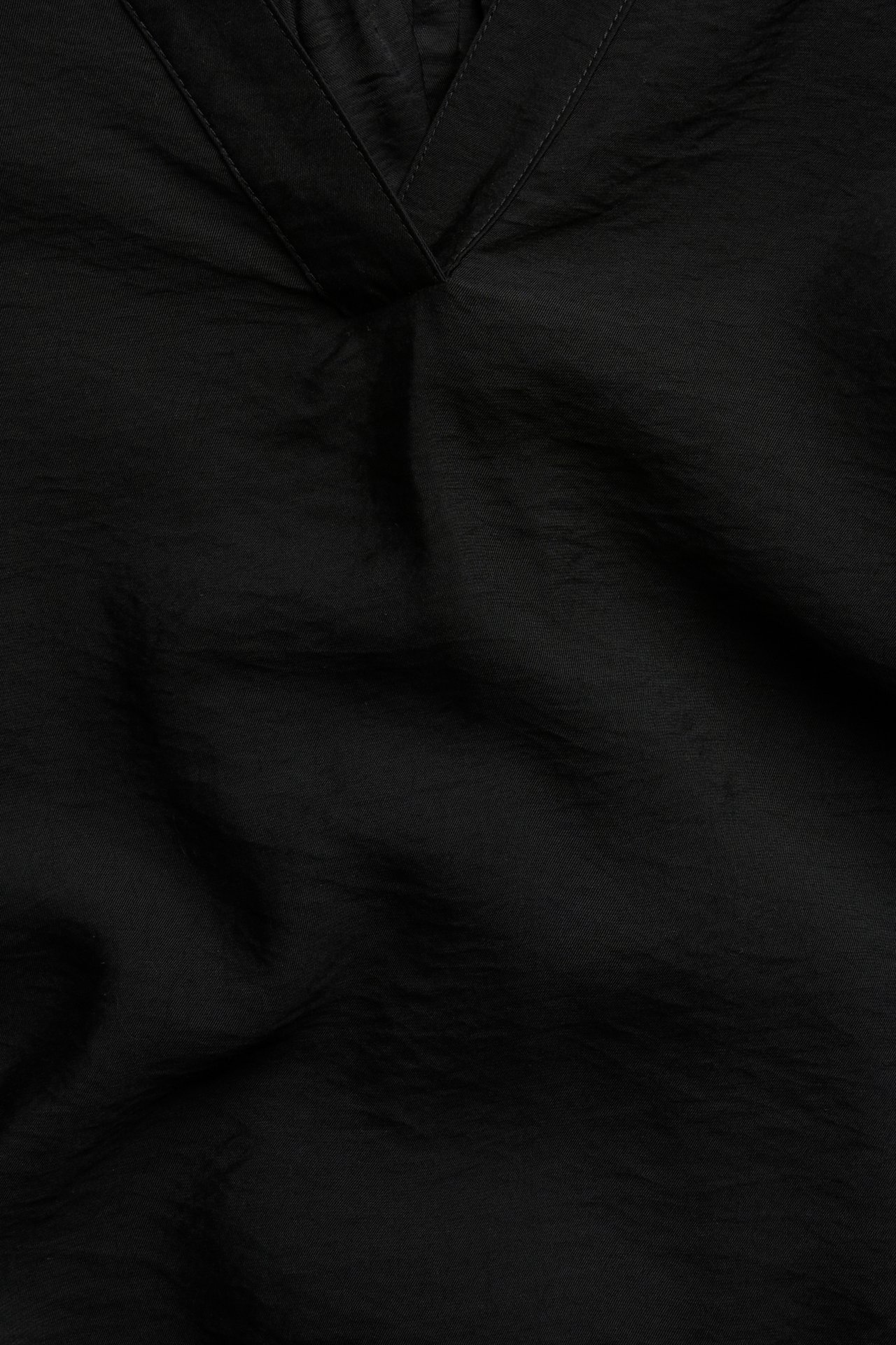 Lähikuva mustasta pop-over-puserosta, jossa V-pääntie, 3/4-puffihihat ja kuvioitu viskoosi-polyamidikangas.