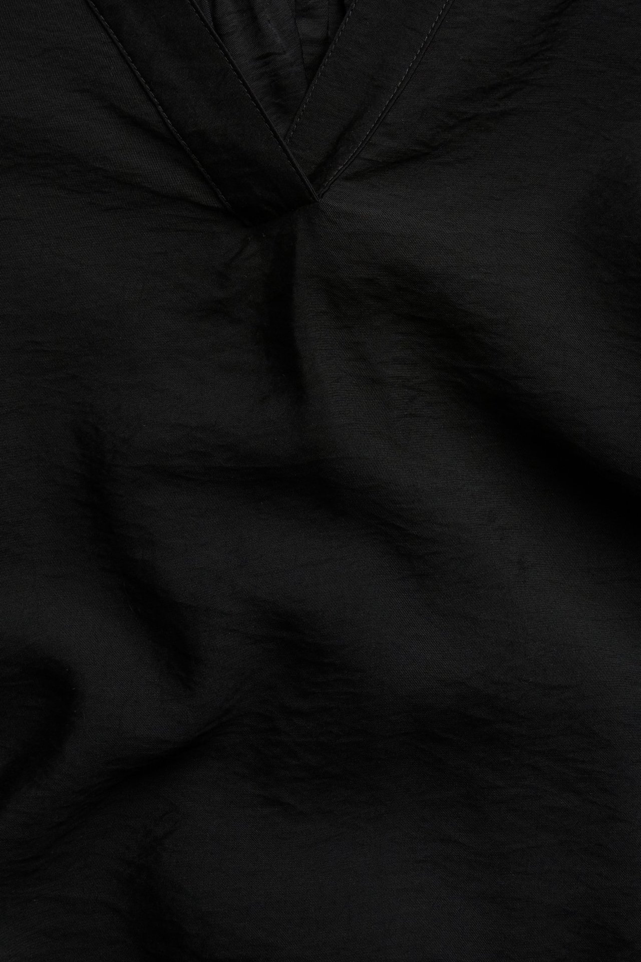 Lähikuva mustasta pop-over-puserosta, jossa V-pääntie, 3/4-puffihihat ja kuvioitu viskoosi-polyamidikangas.