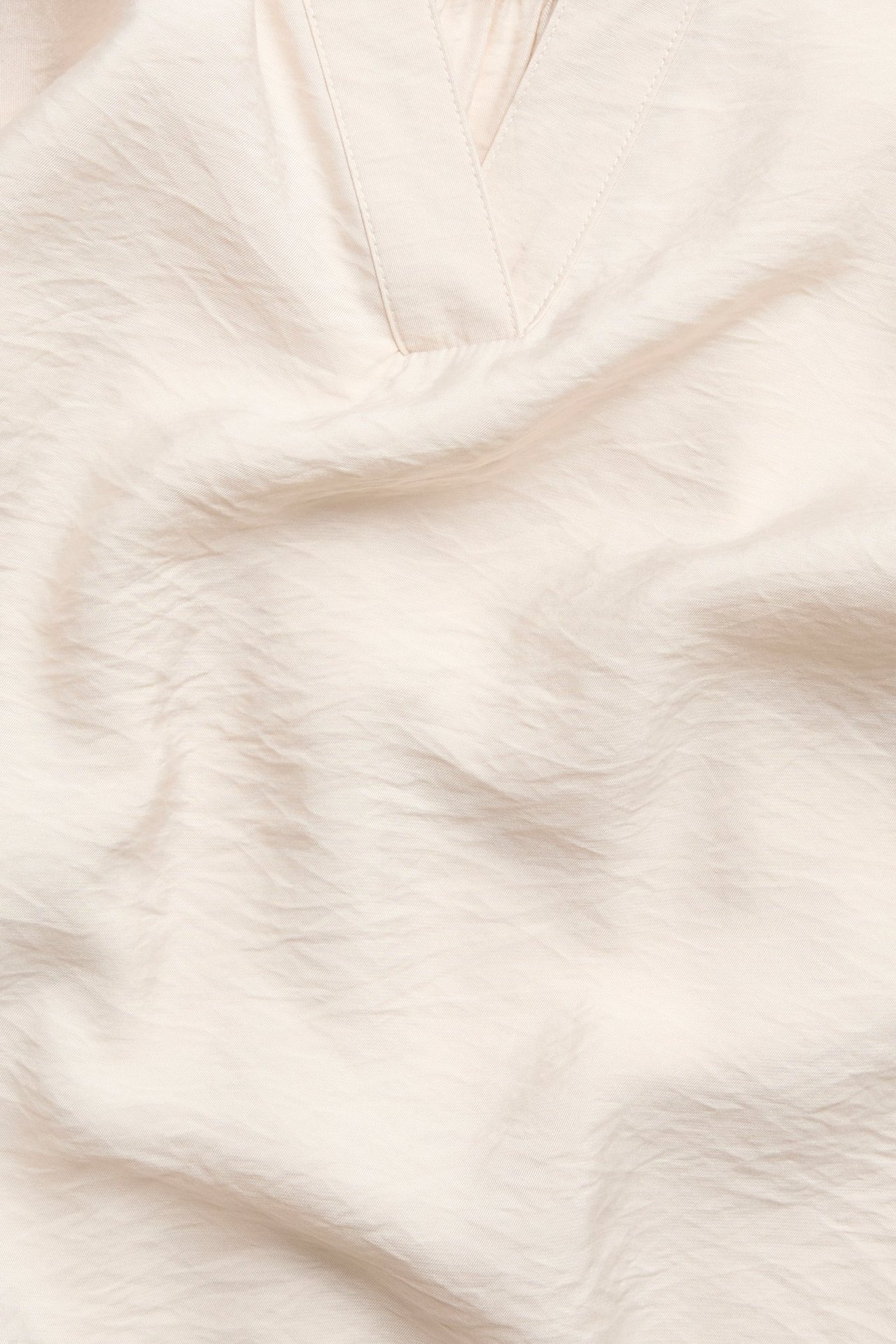 Lähikuva vaaleanbeigestä V-kaula-aukkoisesta puserosta, jossa on kevyesti rypytetty pinta.