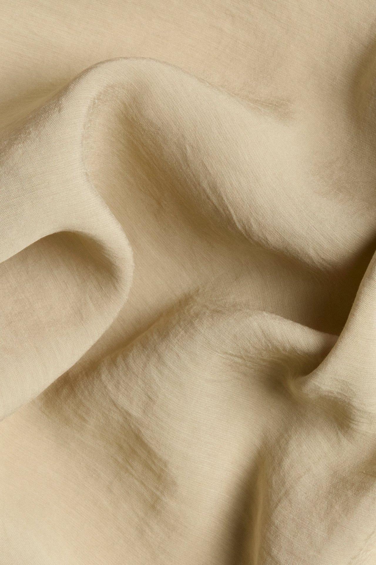 Zbliżenie beżowej, jednolitej, jedwabistej tkaniny z pięknym połyskiem i miękkimi fałdami.