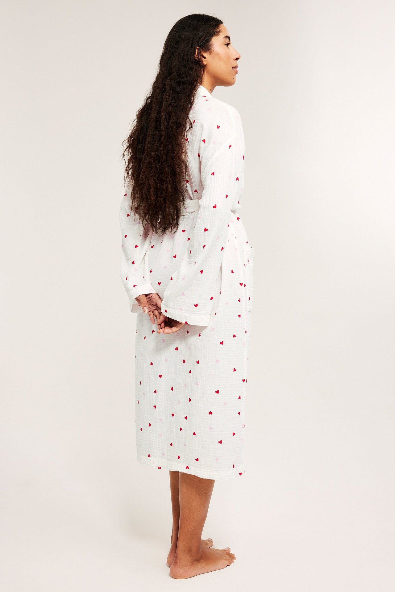 Widok z boku kobiety w écru bawełnianym szlafroku w czerwone serca, z odpinanym paskiem.