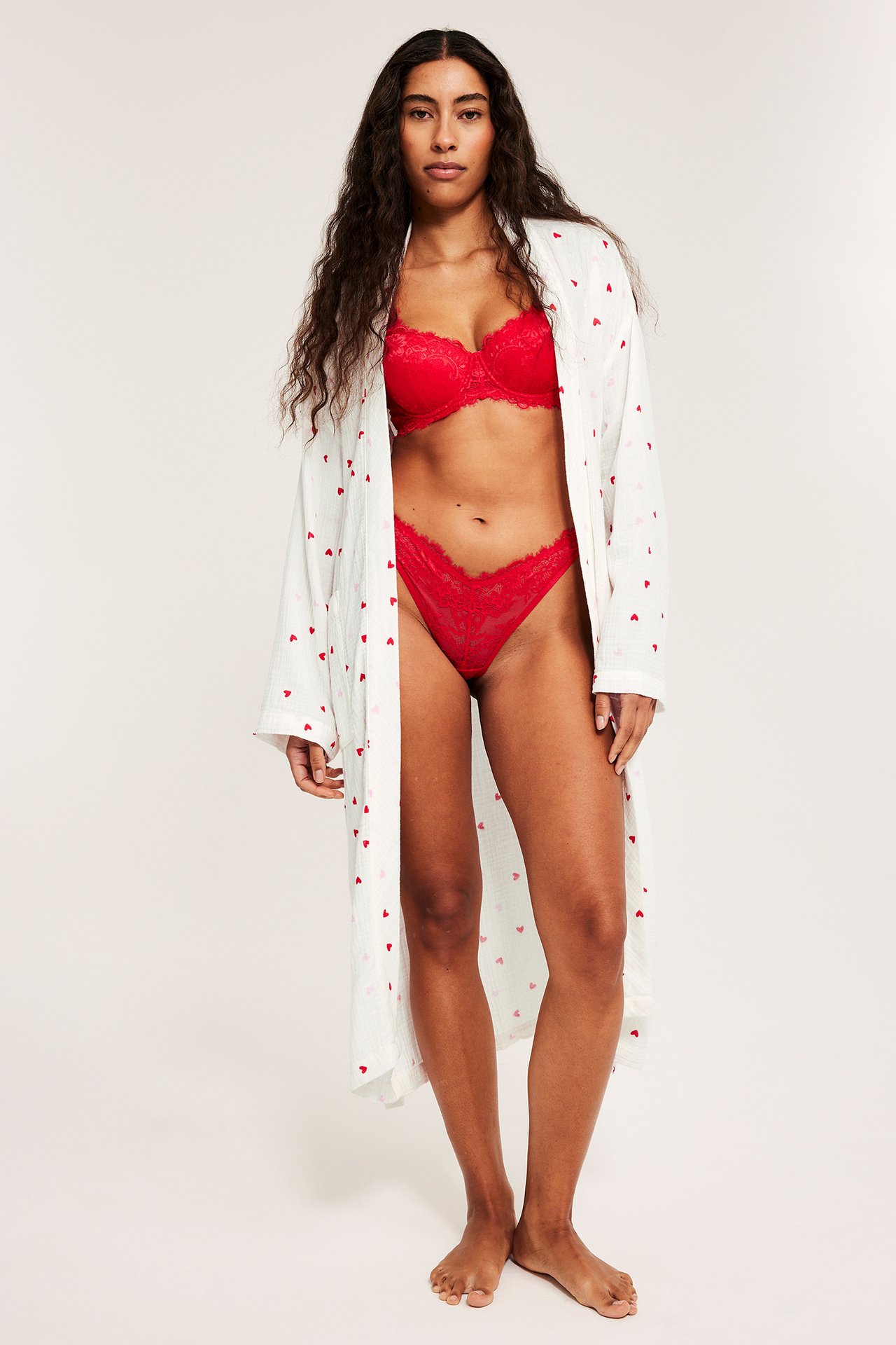 Kobieta z przodu: otwarty ecru bawełniany szlafrok w serca, na czerwonym koronkowym biustonoszu i majtkach.