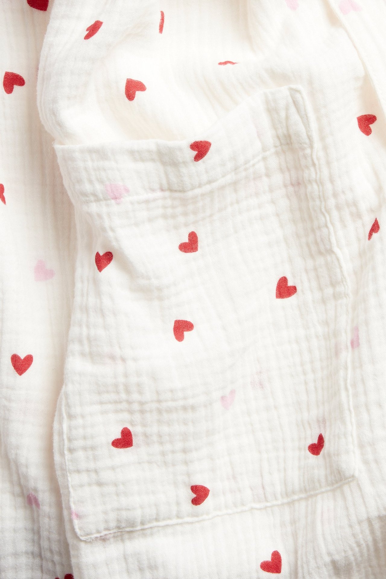 Zbliżenie na ecru dwuwarstwowy bawełniany szlafrok z czerwonym wzorem w serca i przednią kieszenią.
