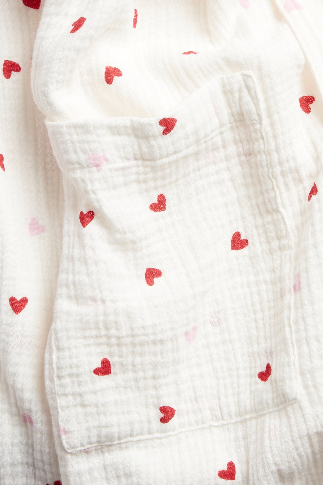 Zbliżenie na ecru dwuwarstwowy bawełniany szlafrok z czerwonym wzorem w serca i przednią kieszenią.