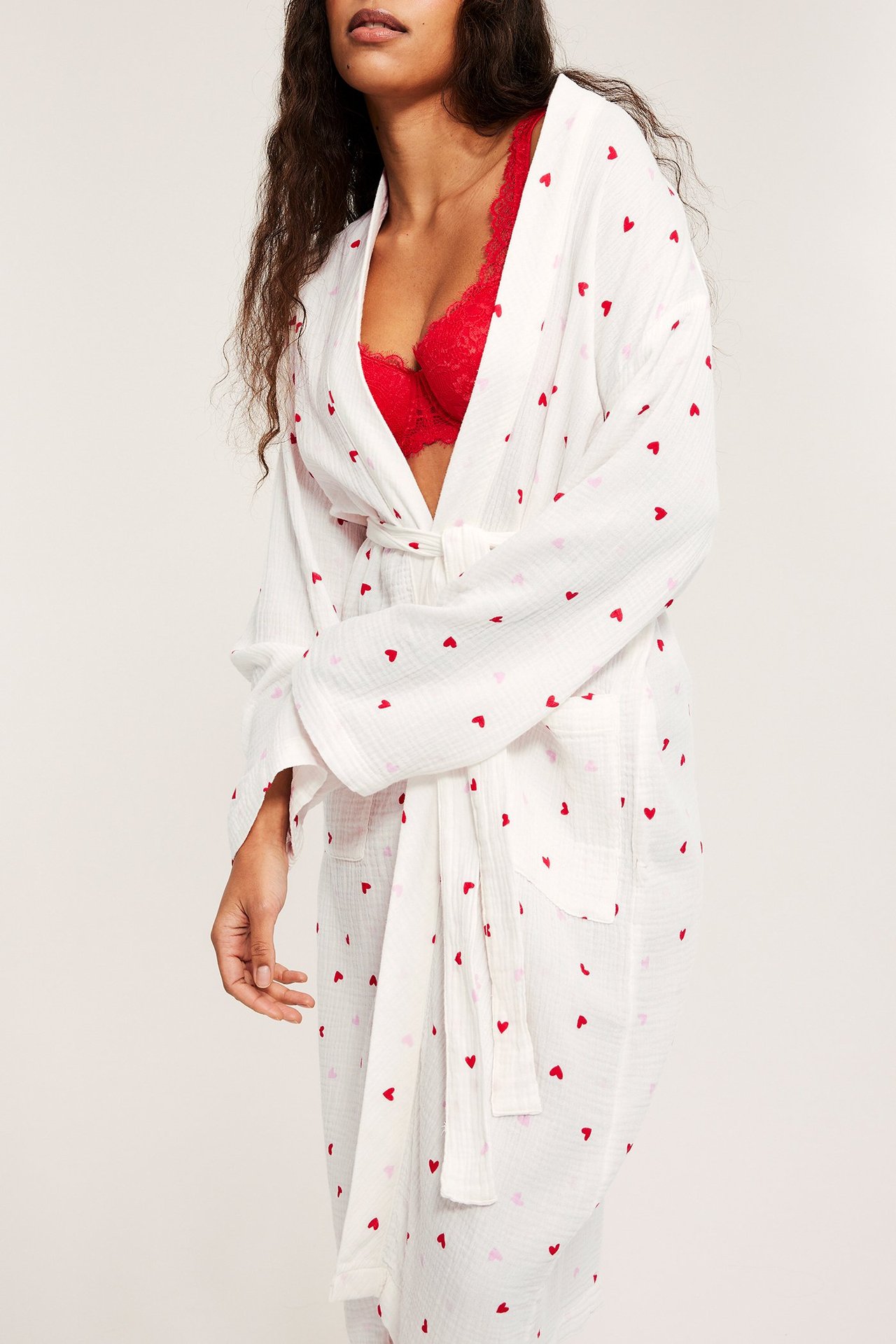 Widok z przodu: kobieta w ecru bawełnianym szlafroku w serca, wiązanym, na czerwonym biustonoszu.