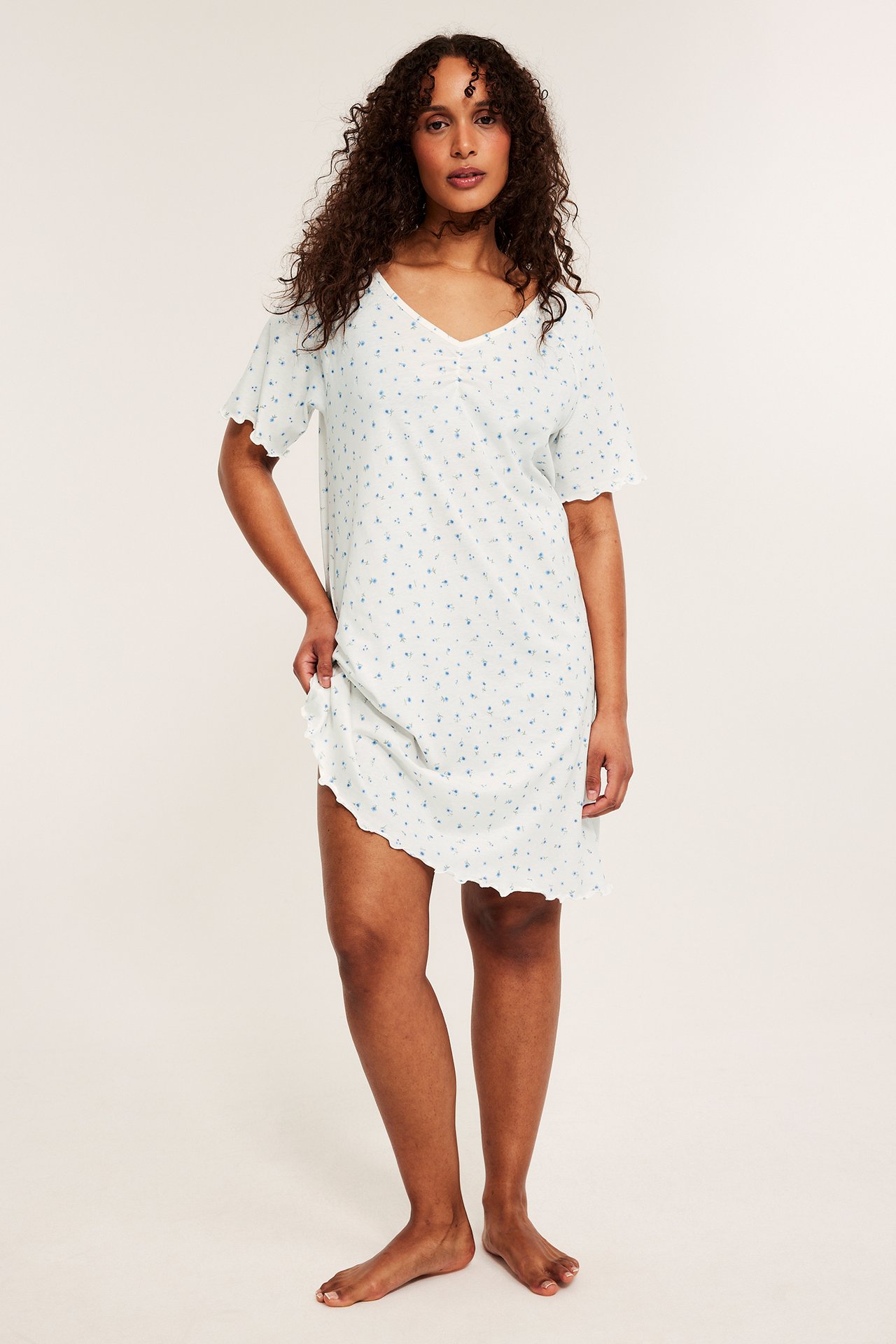 Frontvy av kvinne i lys blåmønstret bomullsnattkjole med dyp V-hals og bølgete kanter.