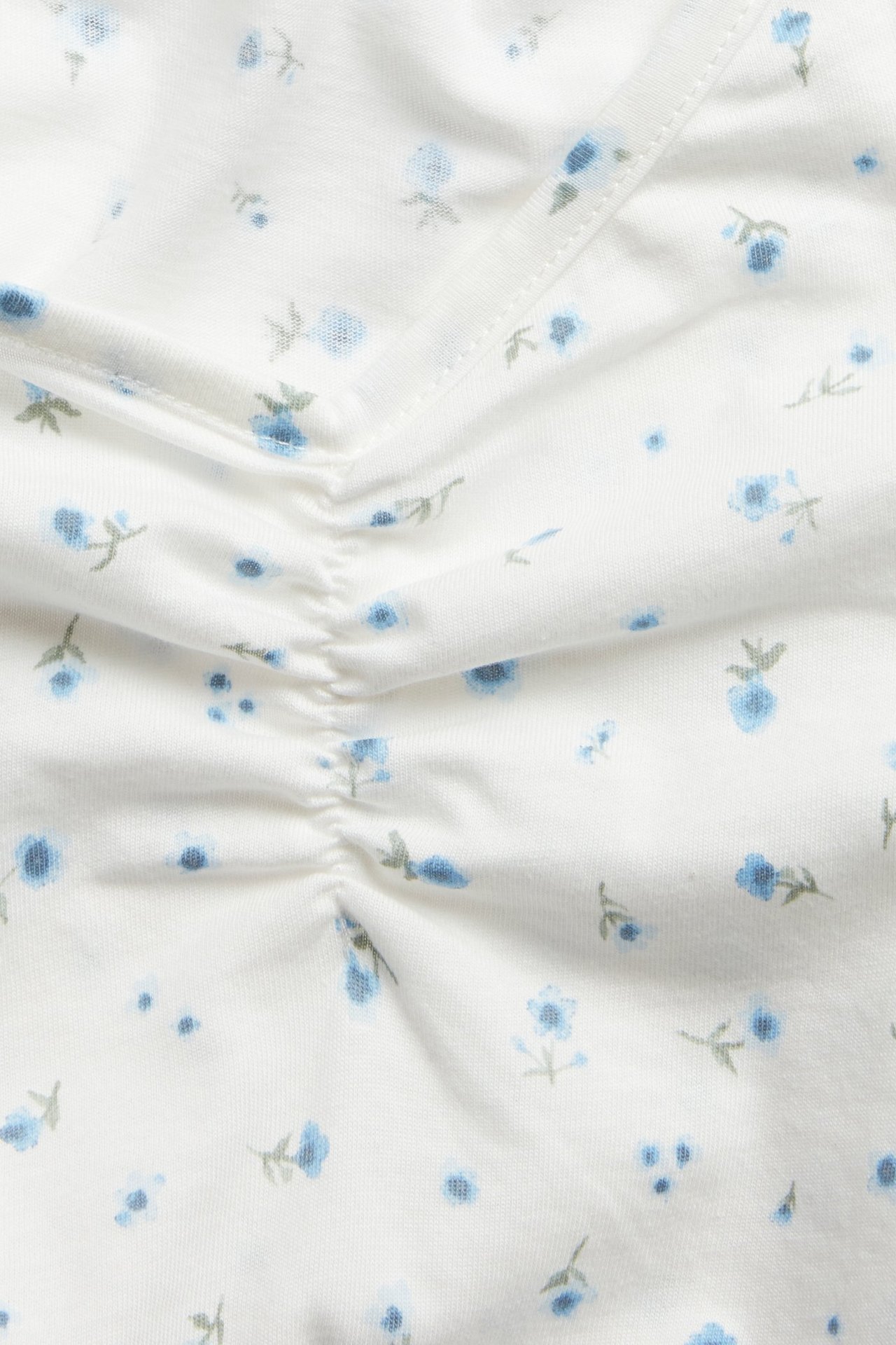 Zbliżenie na białą koszulę nocną z jasnoniebieskim kwiatowym wzorem i marszczeniem z przodu.