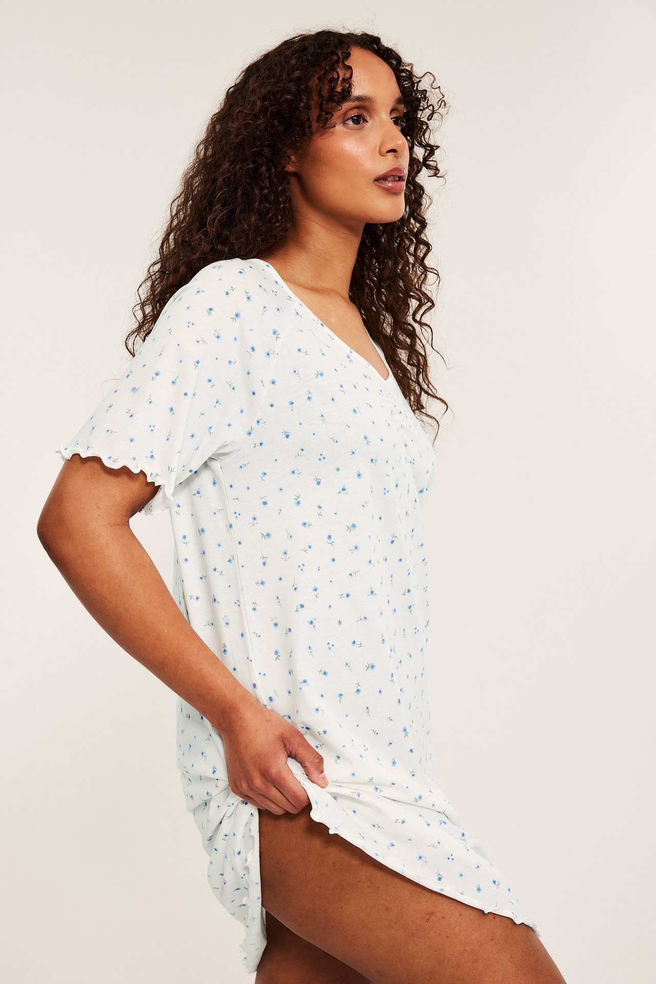 Sidovy av en kvinna i vitt bomullstrikå nattlinne med ljusblått blommigt mönster och vågiga kanter.