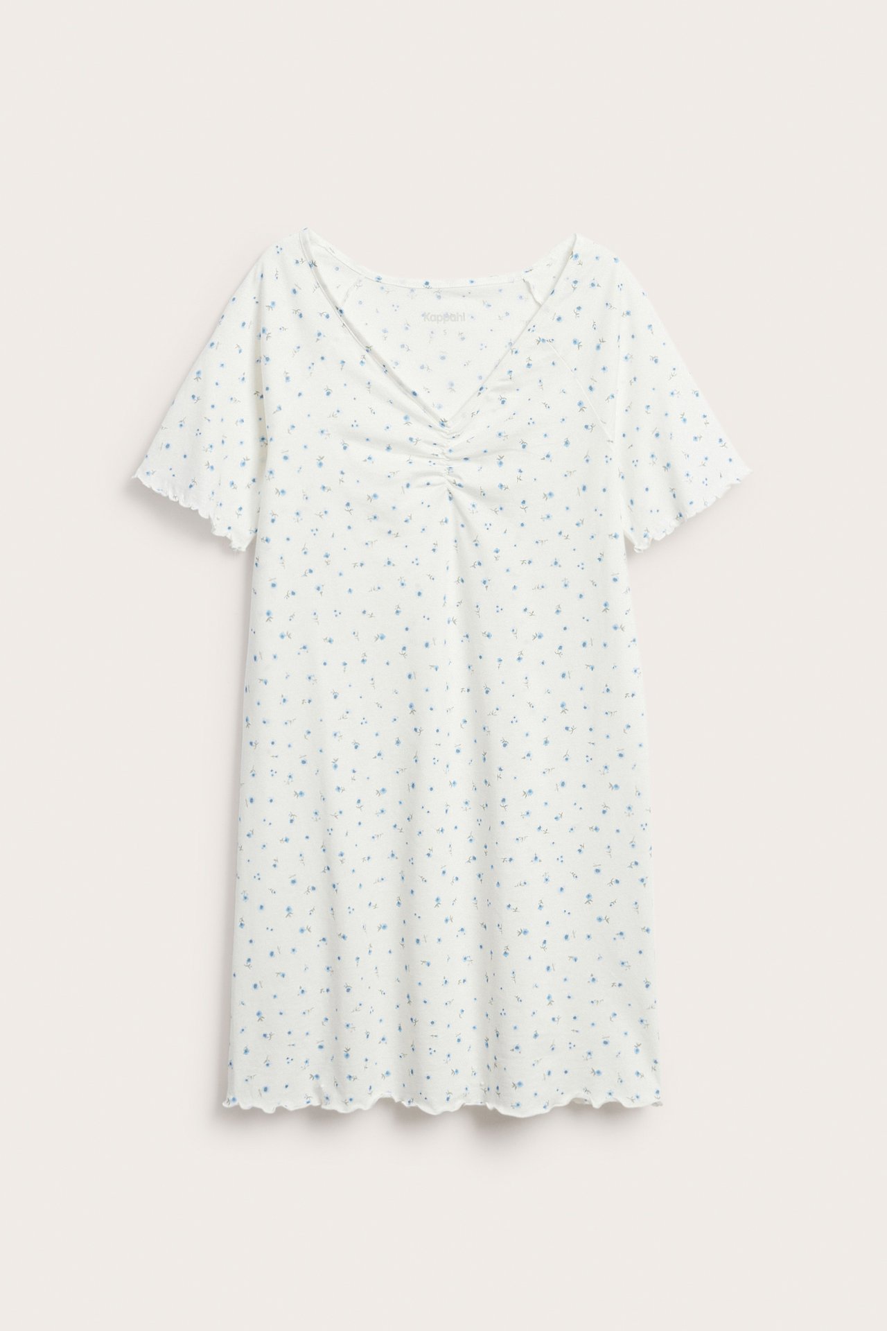 Edestä: Valkoinen trikooyömekko, vaaleansininen kukkakuvio, lyhyet aaltoilevat hihat ja rypytetty V-pääntie.