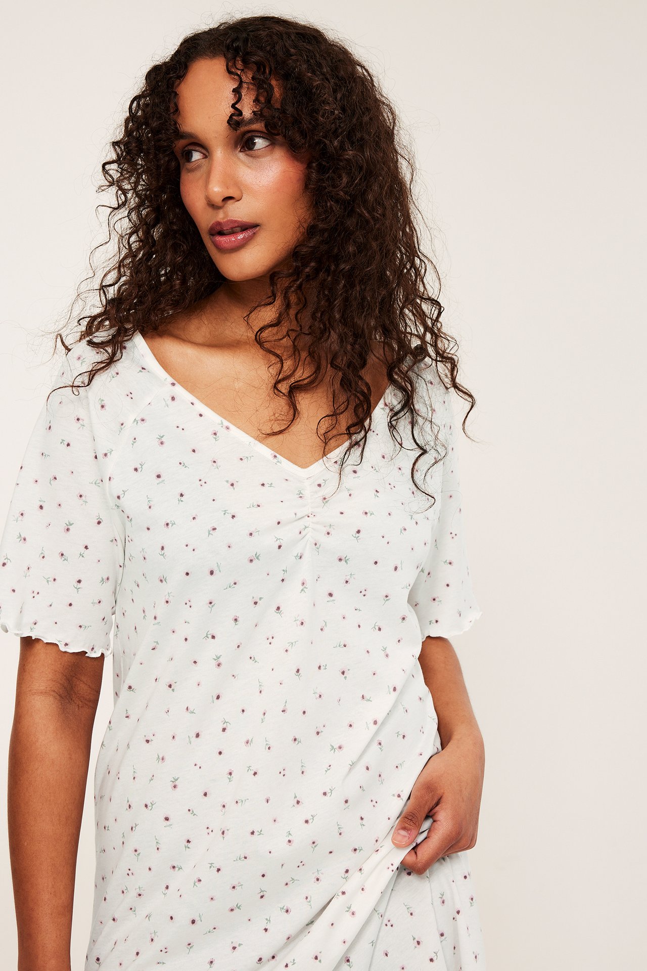 Forfra: Kvinne i hvit nattkjole i bomullsjersey med rosa blomstermønster og rynket V-hals.