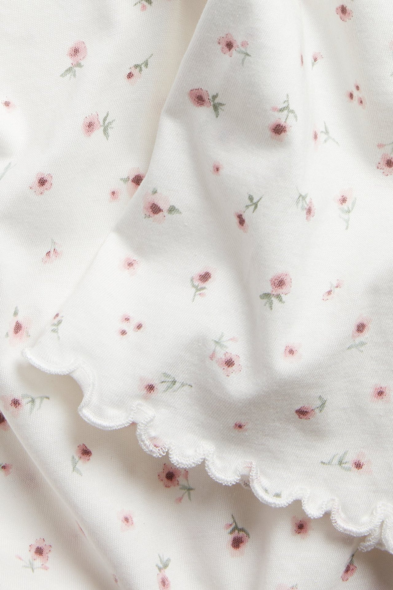Zbliżenie na białą bawełnianą tkaninę koszuli nocnej z różowym kwiatowym wzorem i falistym brzegiem.