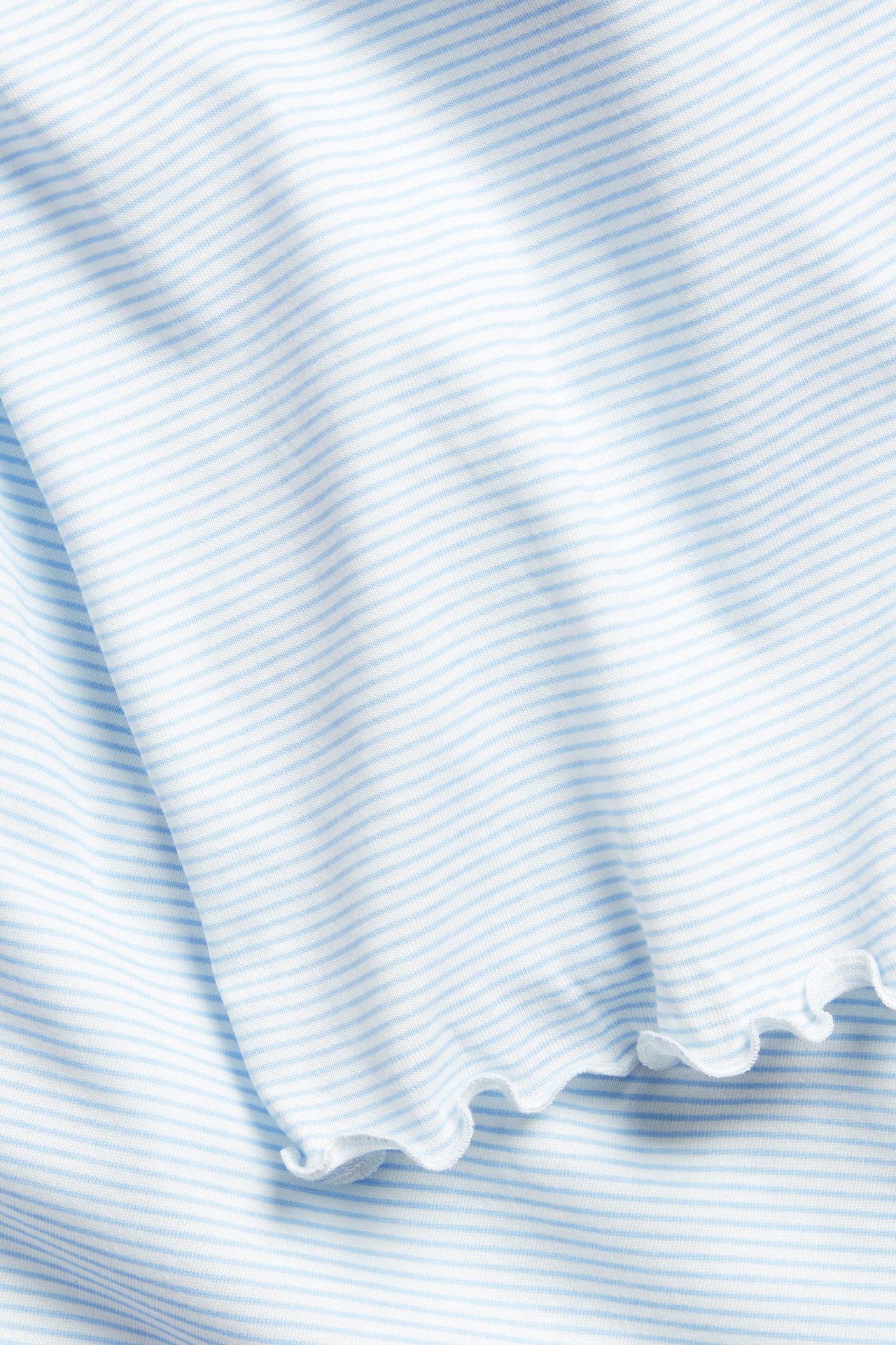 Nærbilde av et lyseblått og hvitstripet nattkjolestoff i bomullstrikot med en rynkekant.
