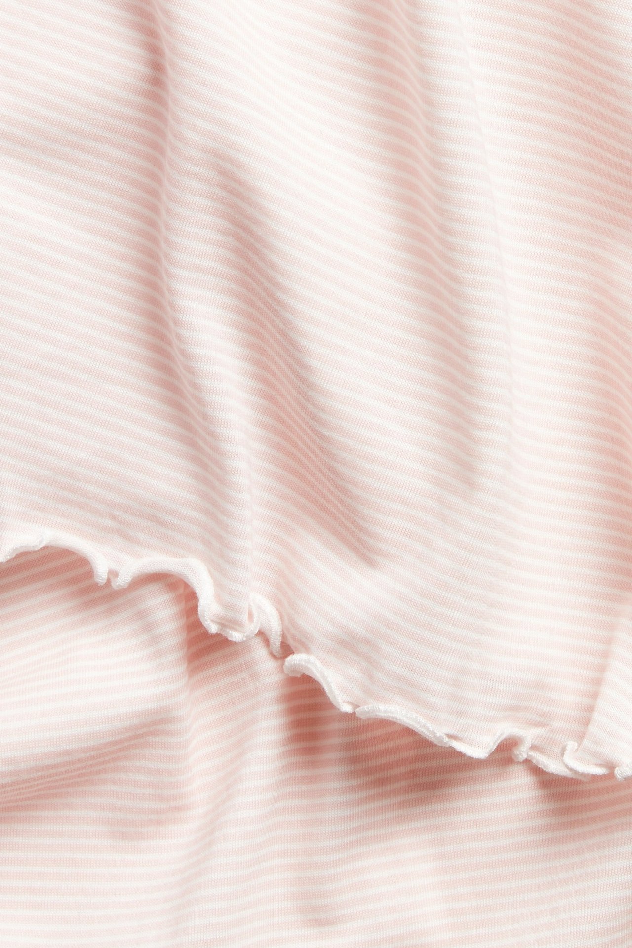 Zbliżenie różowo-białej, bawełnianej koszuli nocnej w paski z falbanowymi krawędziami.