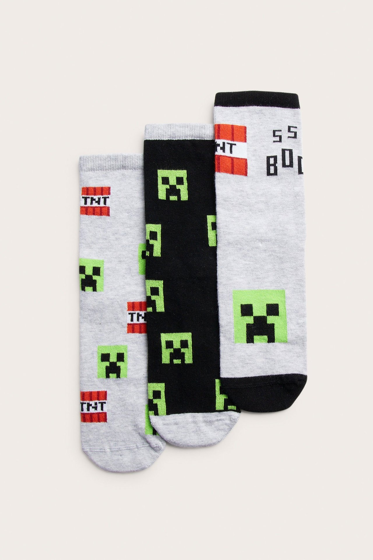 Widok z przodu 3-paku bawełnianych skarpet dziecięcych w jasnoszarym i czarnym kolorze z nadrukami Minecraft Creeper.