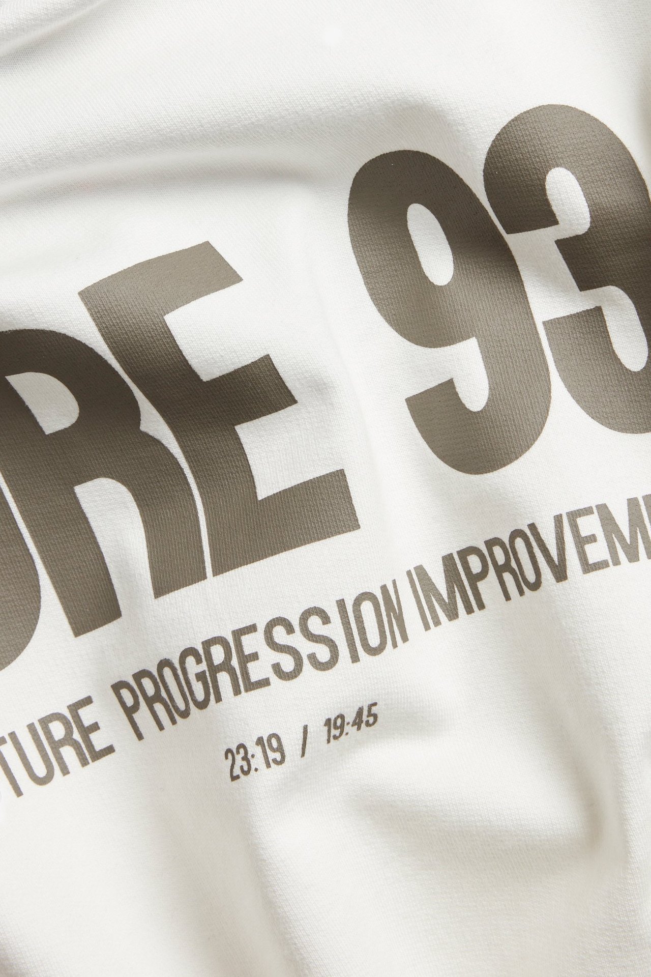 Zbliżenie białego bawełnianego t-shirtu oversize z dużym szarym nadrukiem graficznym "RE 93" i tekstem.