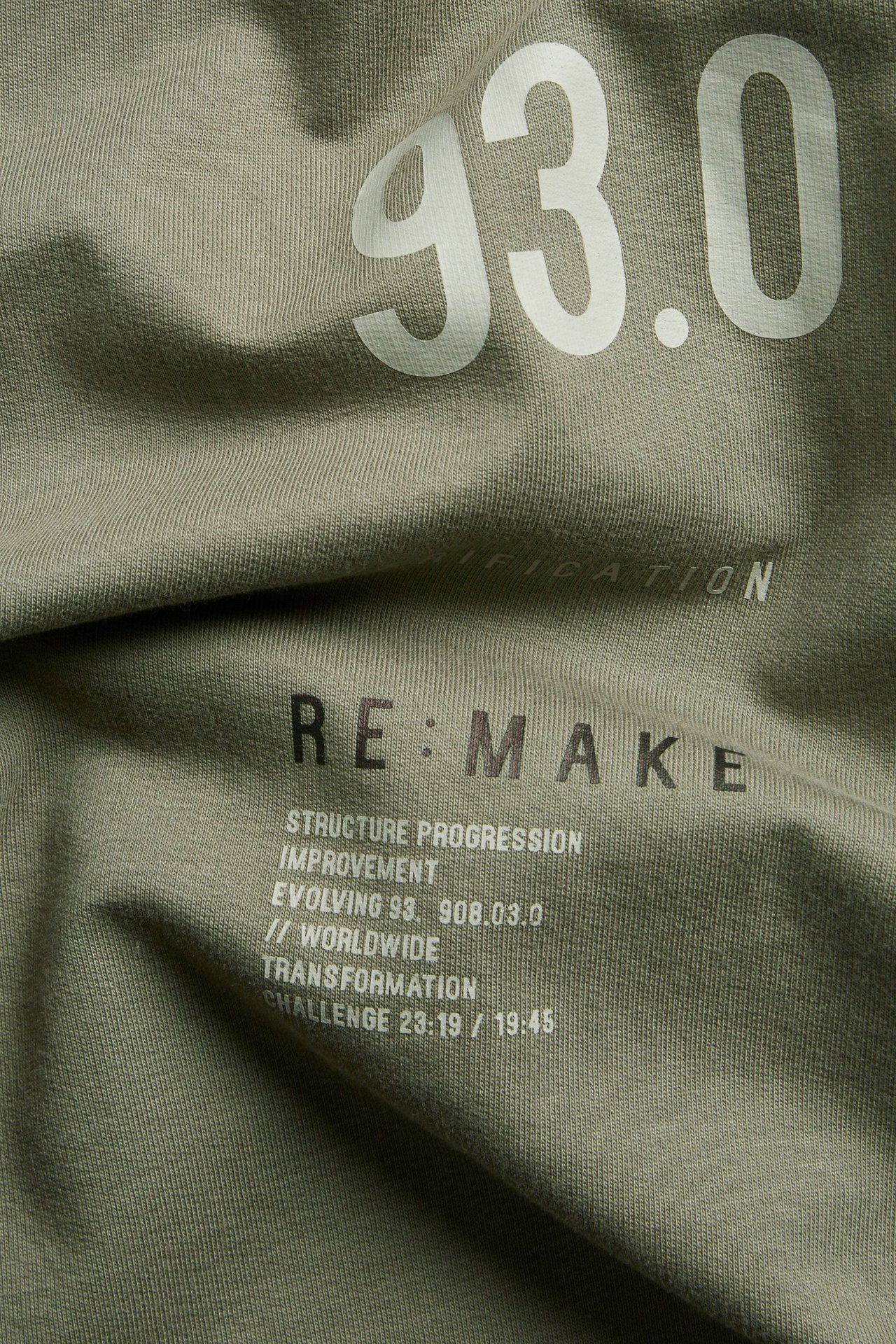 Lähikuva vihreästä ylisuuresta puuvilla-T-paidasta, jossa valkoiset '93.0' ja mustat 'RE:MAKE' tekstit.