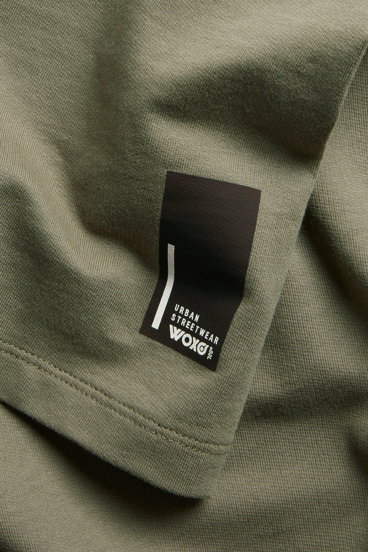 Lähikuva vihreästä oversized puuvilla-T-paidasta, jossa on musta merkki ja valkoinen teksti 'Urban Streetwear Woxo'.