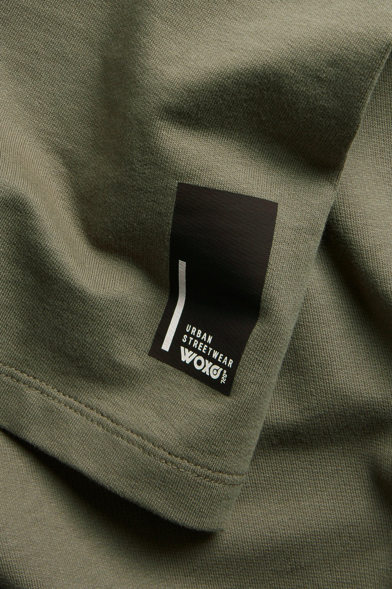 Zbliżenie zielonej bawełnianej koszulki oversize z czarną metką "URBAN STREETWEAR WOXO".