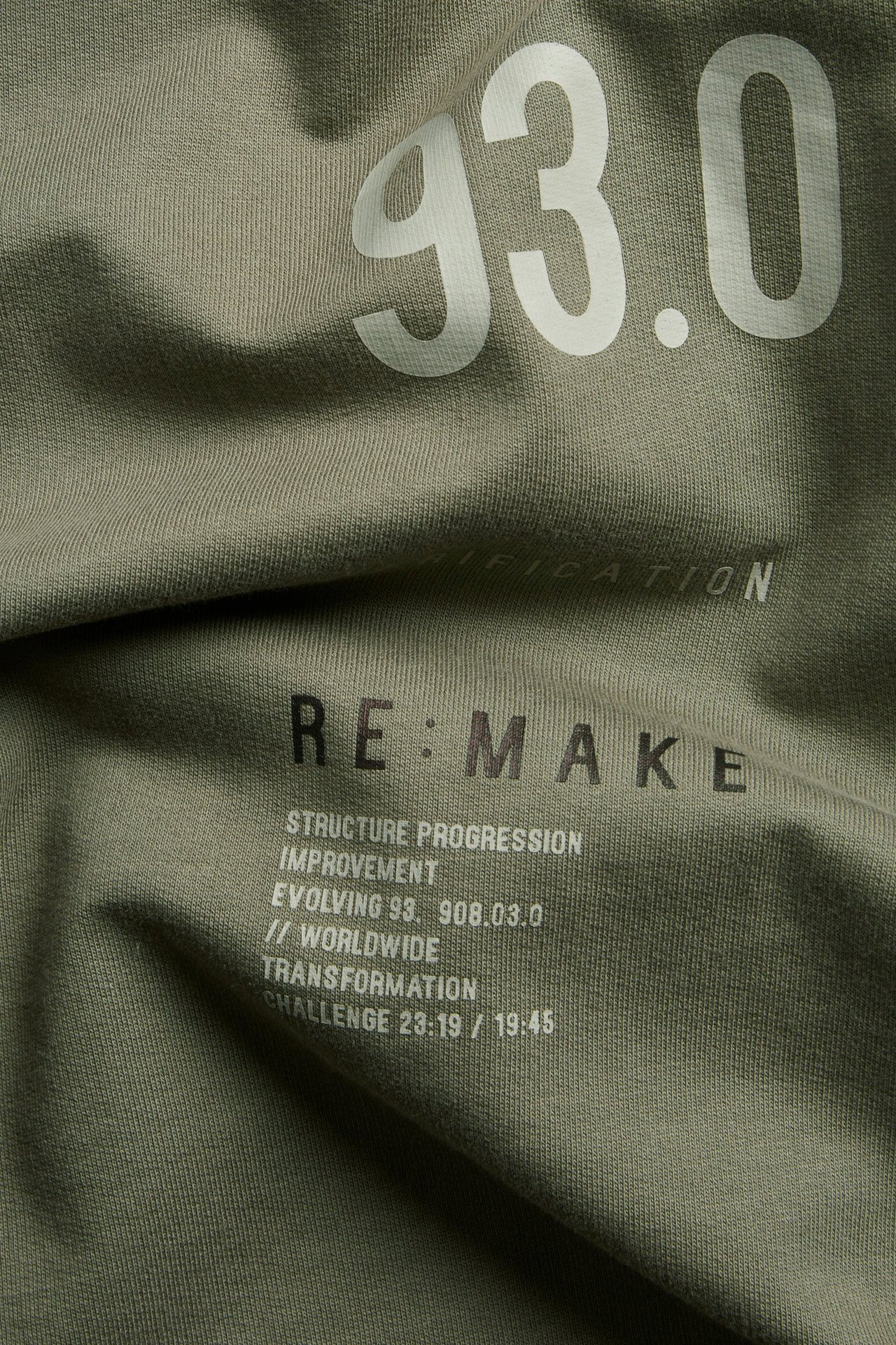 Zbliżenie na zielony bawełniany T-shirt oversize z białymi i czarnymi nadrukami tekstowymi.