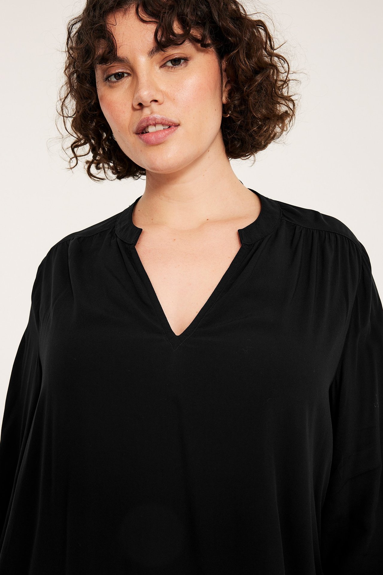 Zbliżenie na kobietę w czarnej bluzce wiskozowej z dekoltem w serek i bufiastymi rękawami.