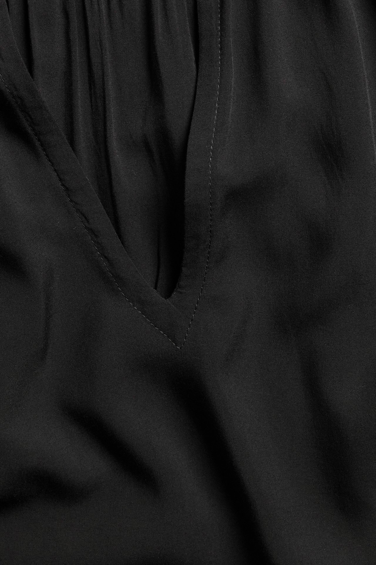 Zbliżenie czarnej bluzki wiskozowej z dekoltem w serek i marszczeniami na karczku.