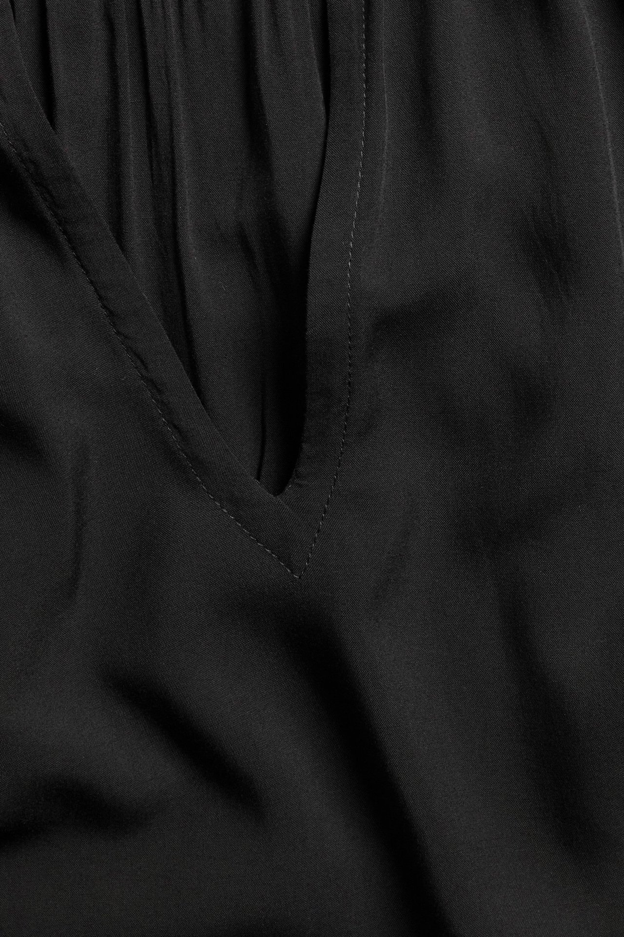 Zbliżenie czarnej bluzki wiskozowej z dekoltem w serek i marszczeniami na karczku.