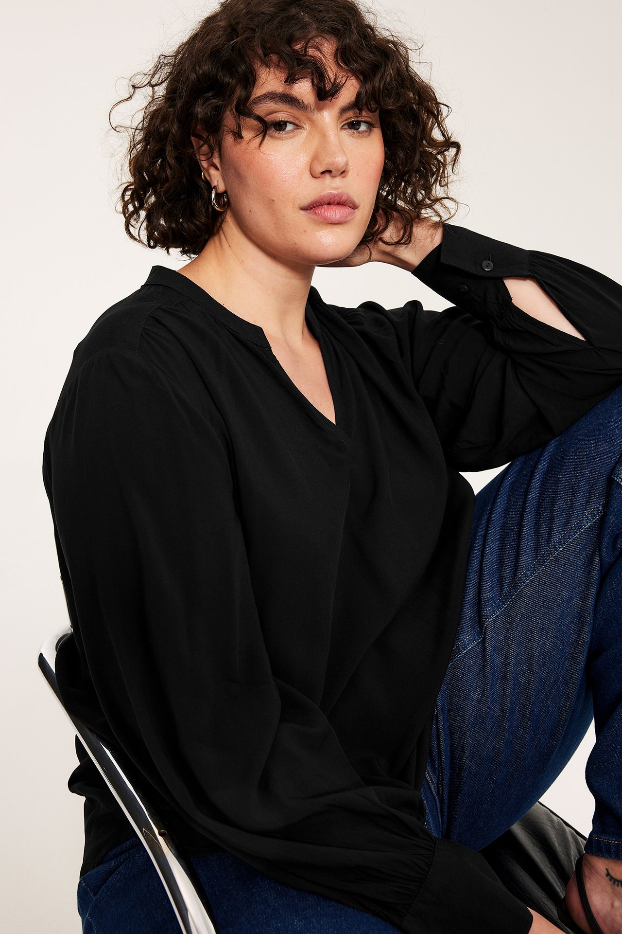 Widok z przodu kobiety w czarnej bluzce z dekoltem w serek, bufiastymi rękawami, granatowych dżinsach i srebrnych kolczykach.
