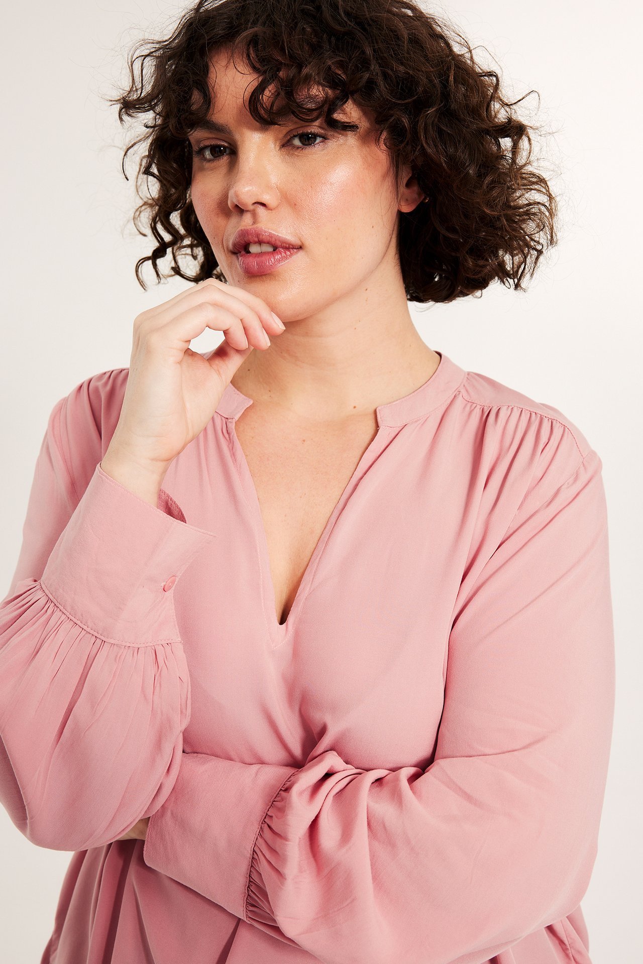 Lähikuva naisesta, jolla on vaaleanpunainen viskoosinen V-aukko-pusero ja pallohihat.