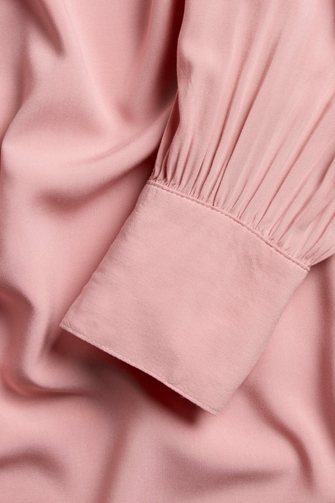 Zbliżenie różowej bluzki z dekoltem w serek, z bufiastym rękawem i szerokim mankietem.
