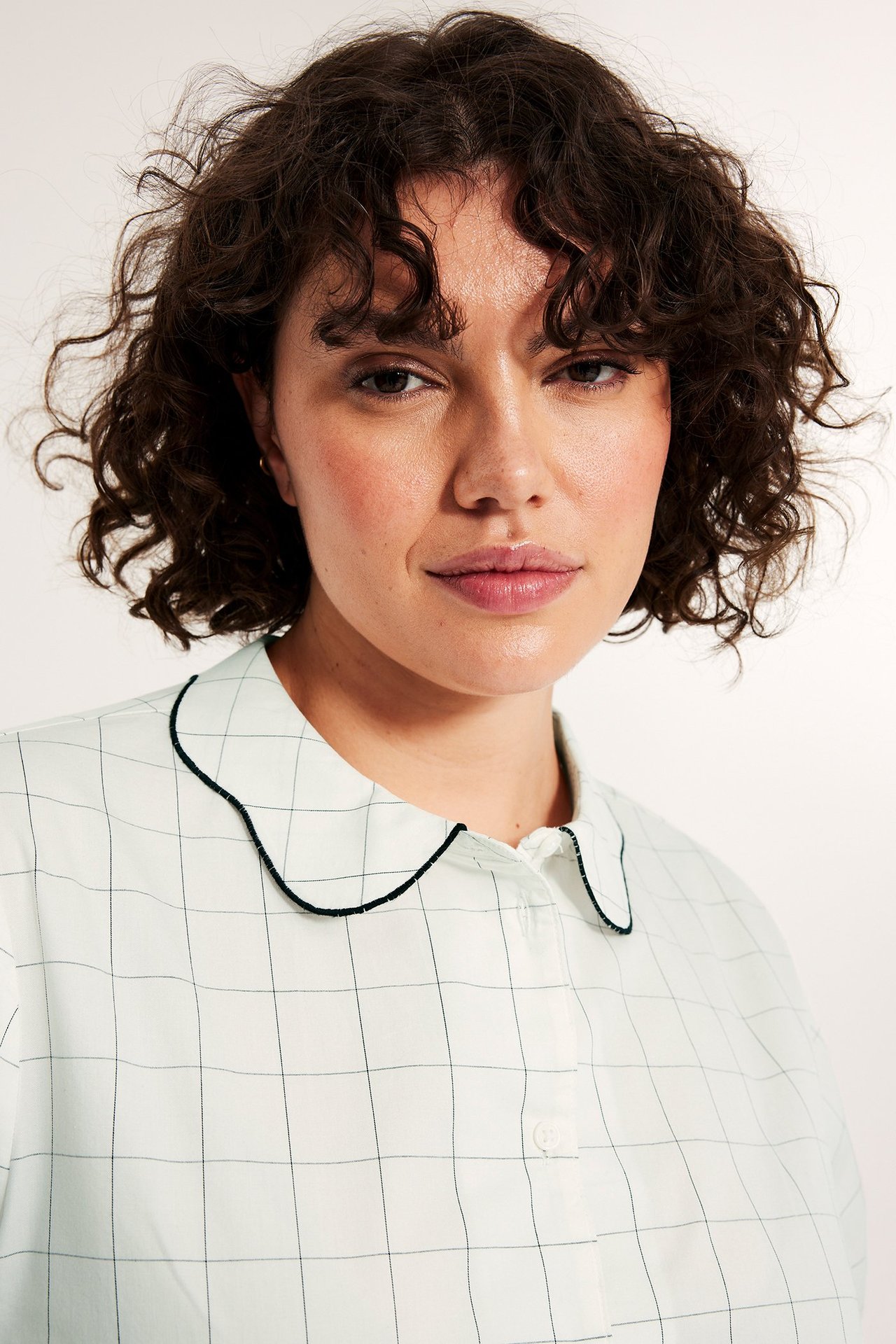 Närbild på kvinna i offwhite rutig bomullsblus med vågig krage och svart kant.