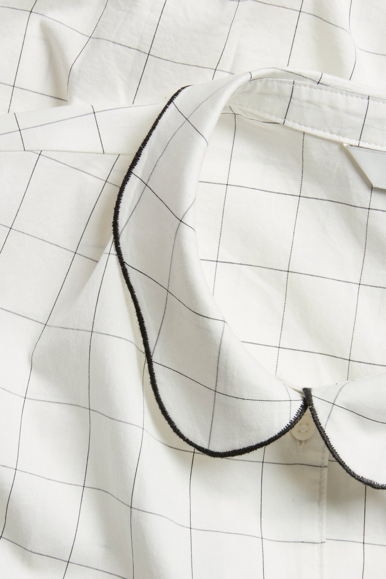 Zbliżenie na off-white bawełnianą bluzkę w czarną kratę z zaokrąglonym, falistym kołnierzykiem.