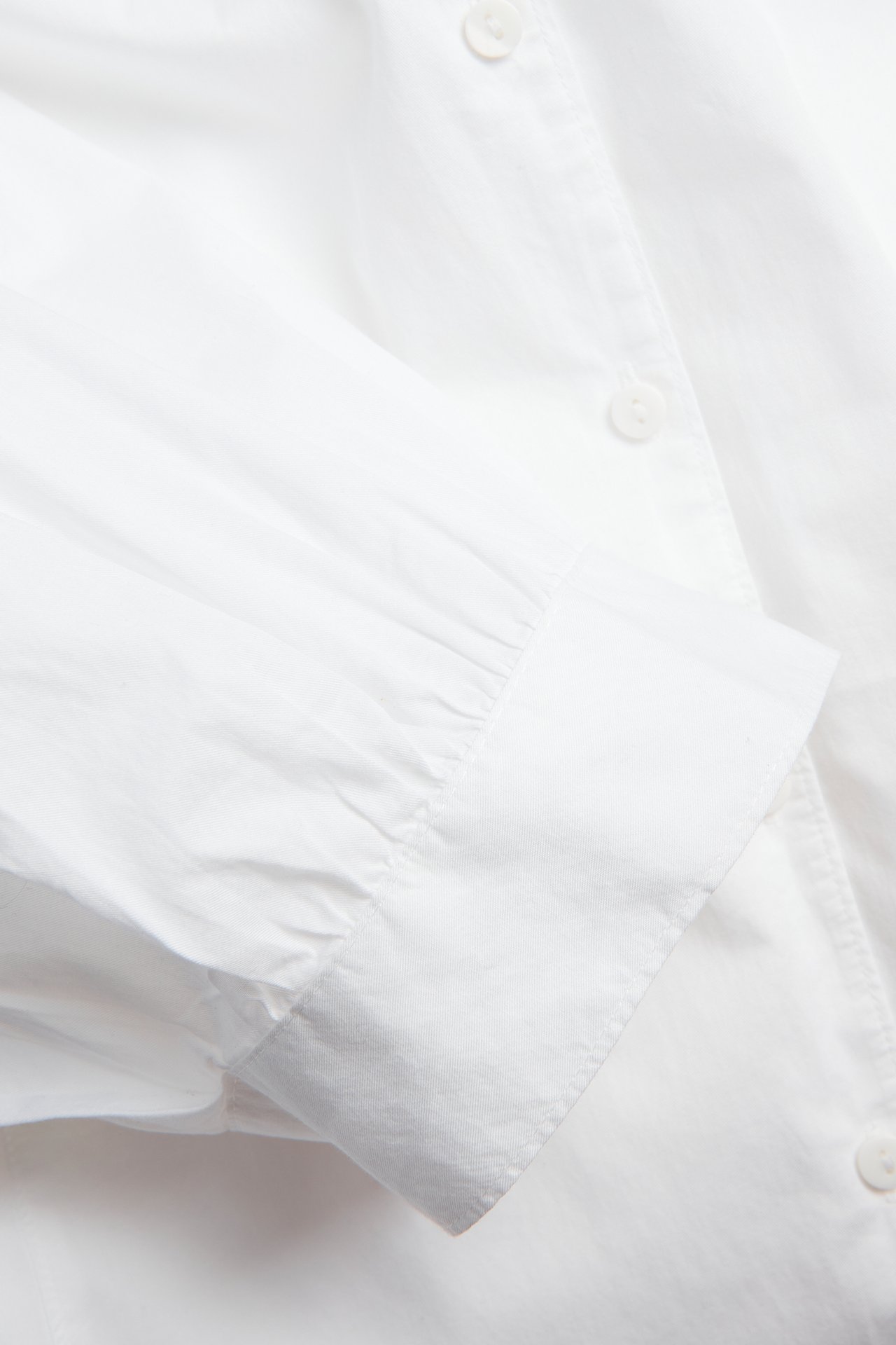Nærbilde av en hvit bomullsbluse med pufferm og mansjett med knapp.