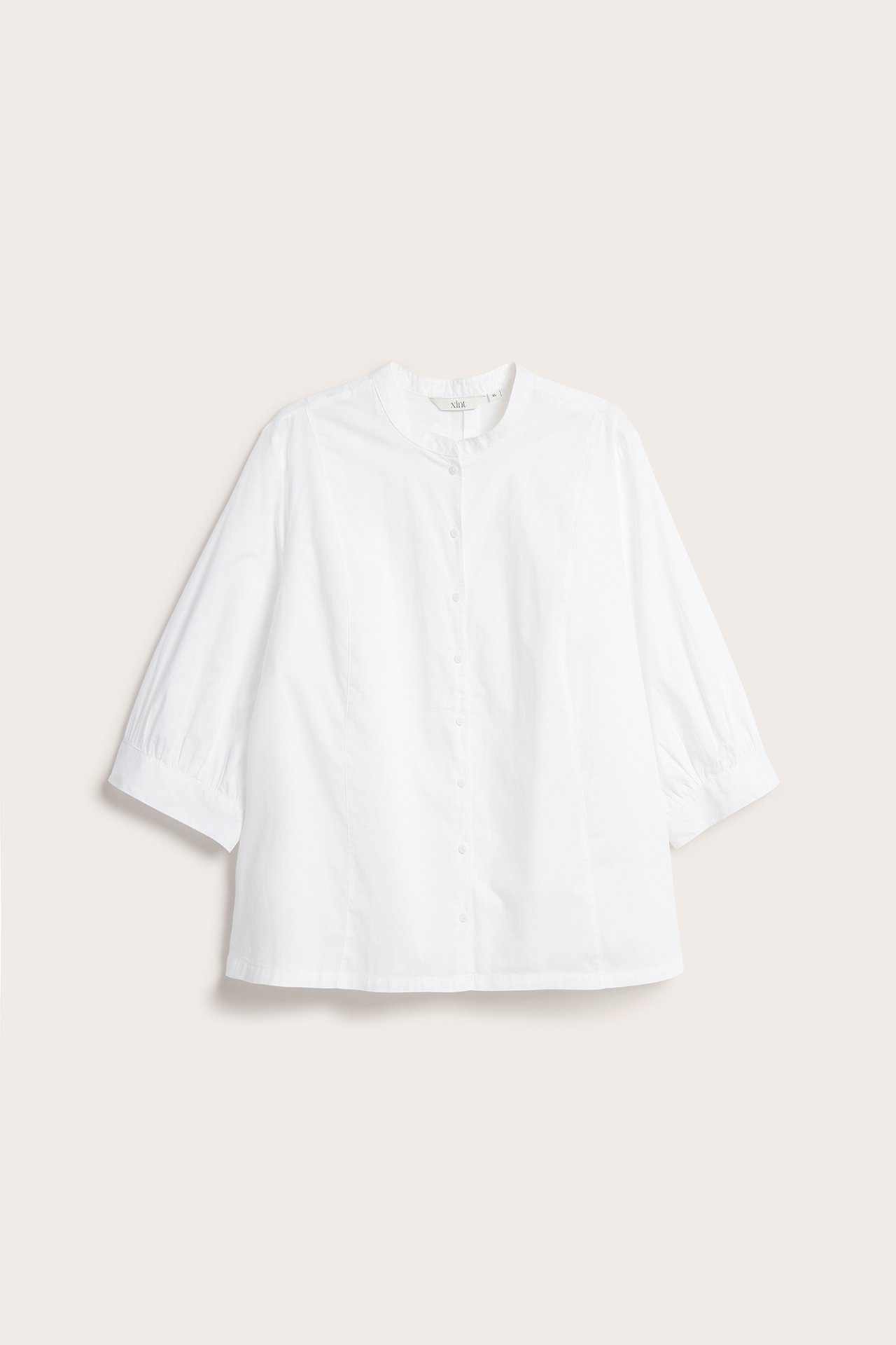 Frontvisning av en hvit, krageløs bomullsbluse med 3/4-puffermer og knappelukking foran.