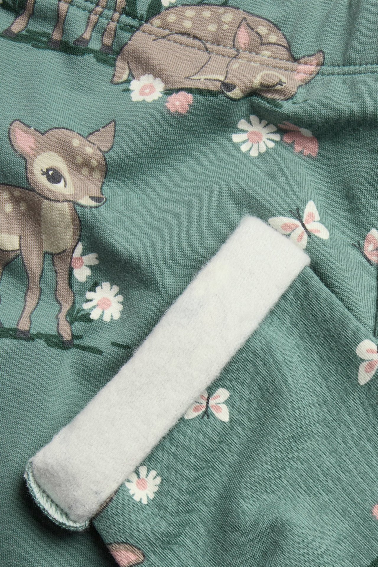 Zbliżenie zielonych wzorzystych ocieplanych legginsów z sarnami, kwiatami, motylami, ukazujące miękkie szczotkowane białe wnętrze.