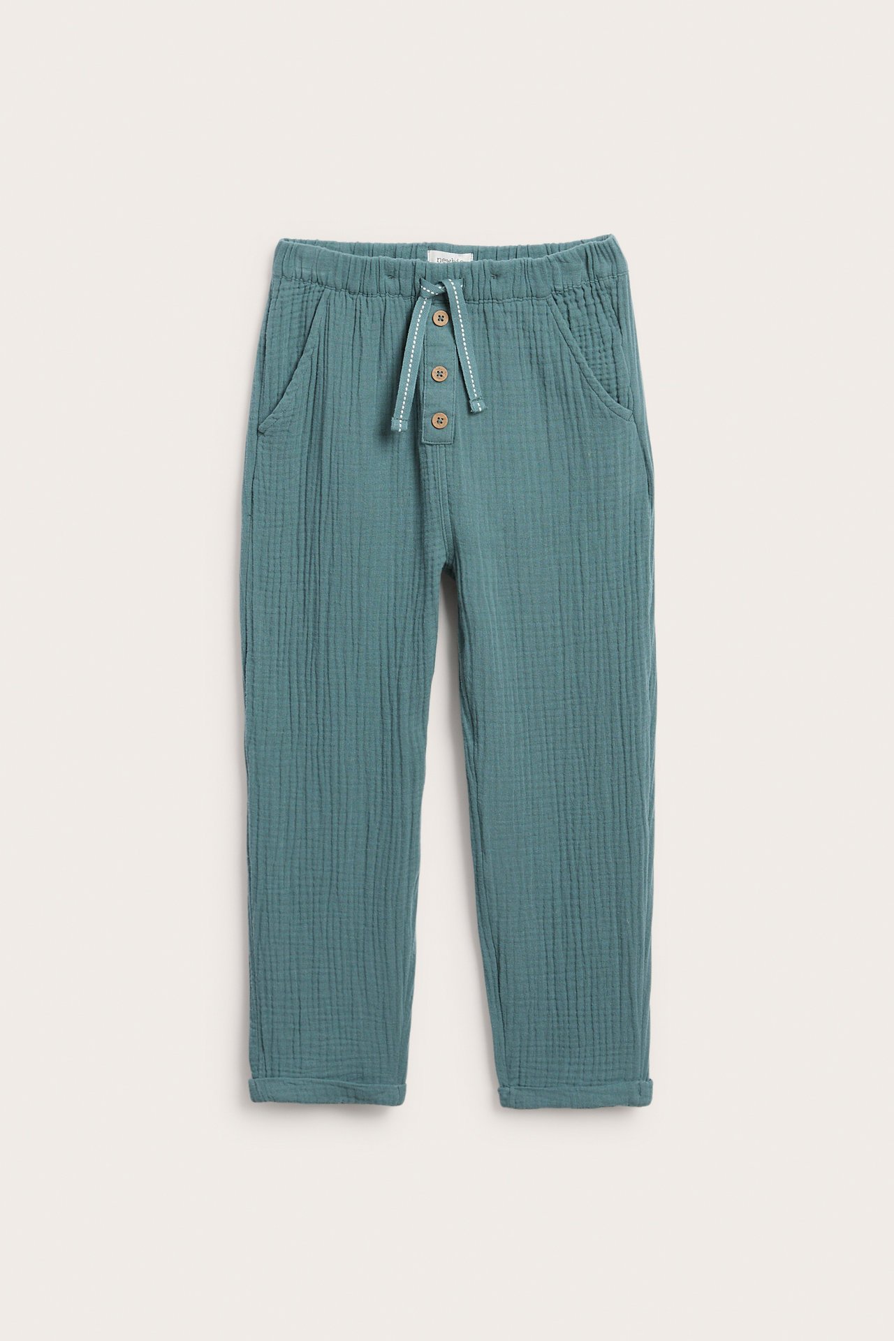 Forfra: Barnas mørk turkise bomullsmuslinbukse med elastisk midje, snøring, frontknapper og opprullede benkanter.