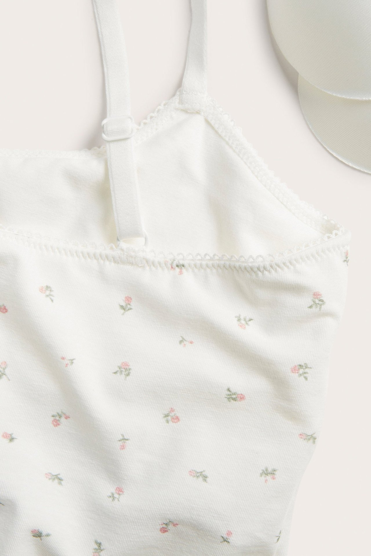 Zbliżenie z góry na biały bawełniany biustonosz bralette z małym różowym wzorem kwiatowym i regulowanym ramiączkiem.