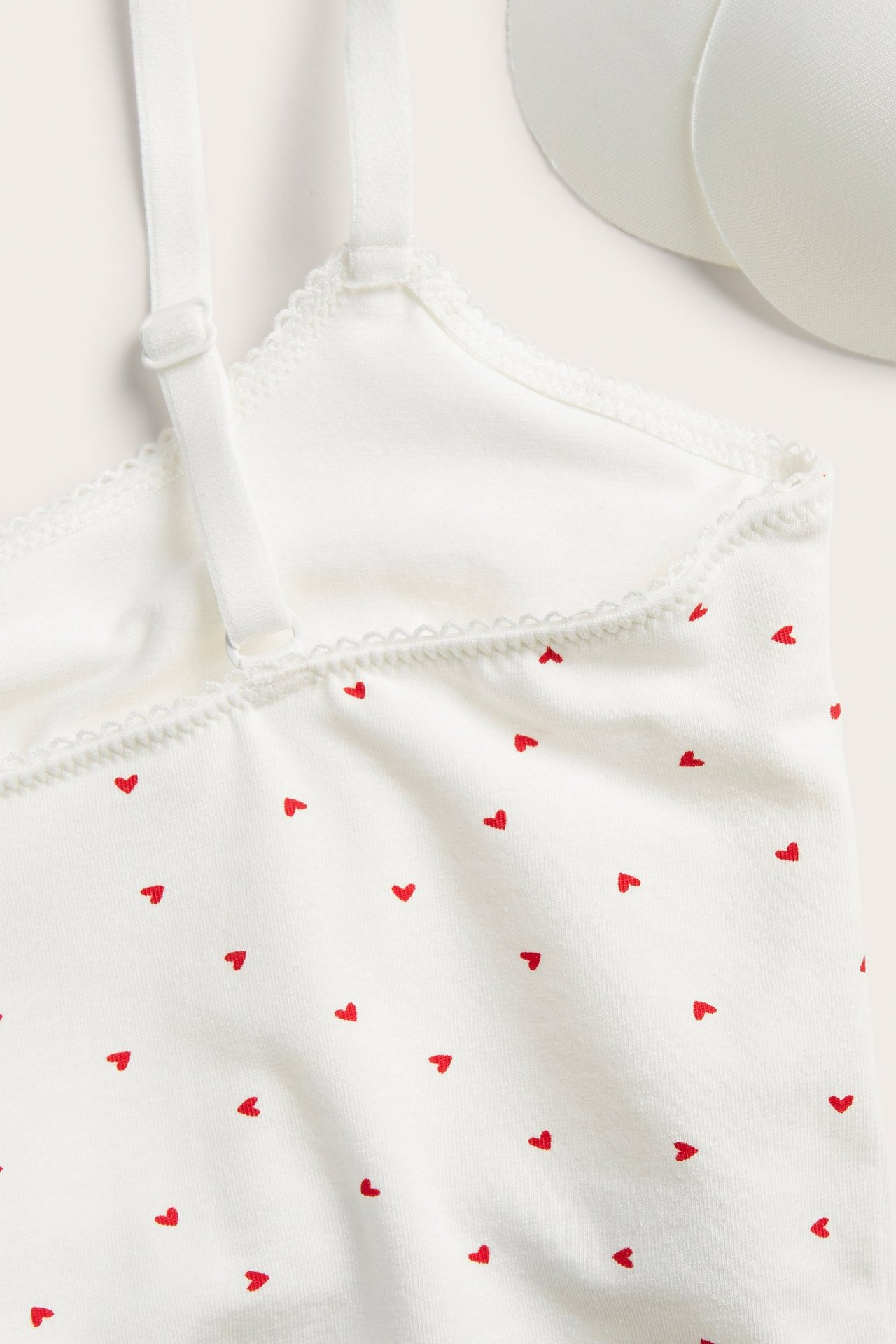 Zbliżenie na ecru bawełniany biustonosz w czerwone serca, z regulowanymi ramiączkami i lamówką picot.