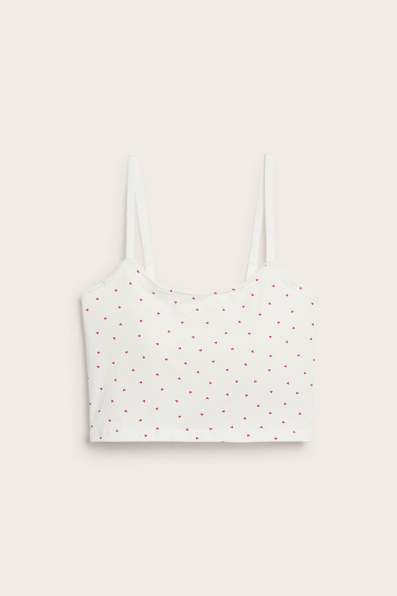 Frontbilde av en offwhite bomullsbralette med tynne stropper og et lite rødt hjertemønster.