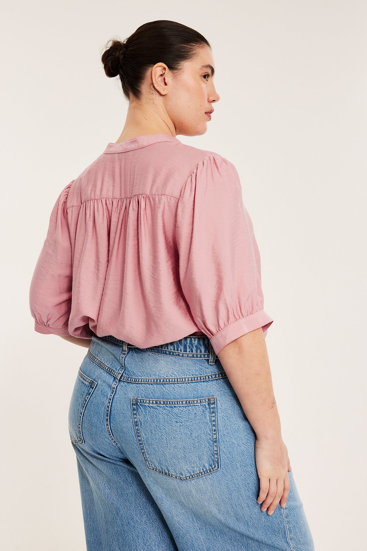 Widok z tyłu kobiety w różowej bluzce popover z rękawami 3/4 i jasnoniebieskich dżinsach.