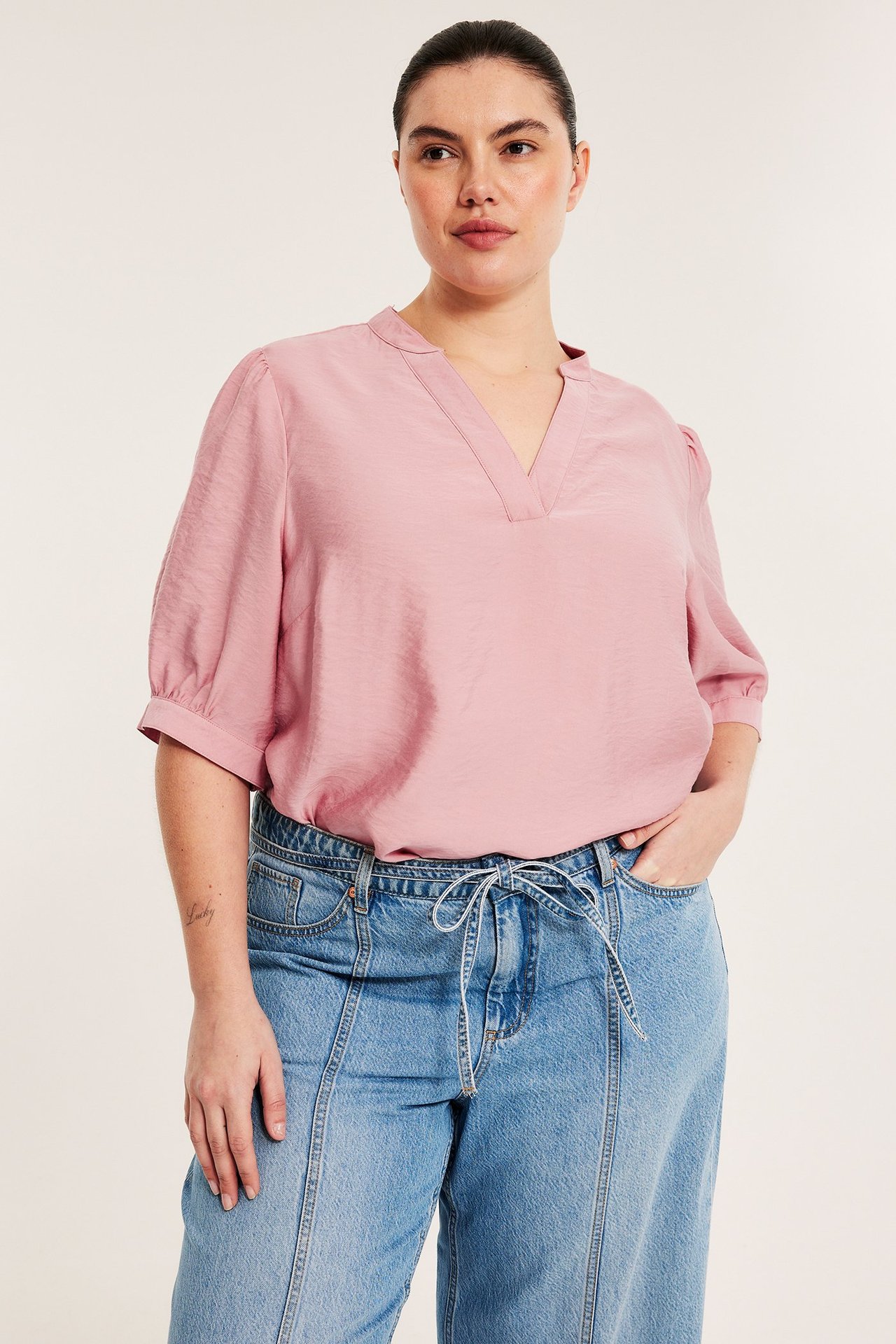 Frontvy av en kvinna i rosa viskosblandad pop-over-blus med V-hals, puffärmar och ljusblå jeans.