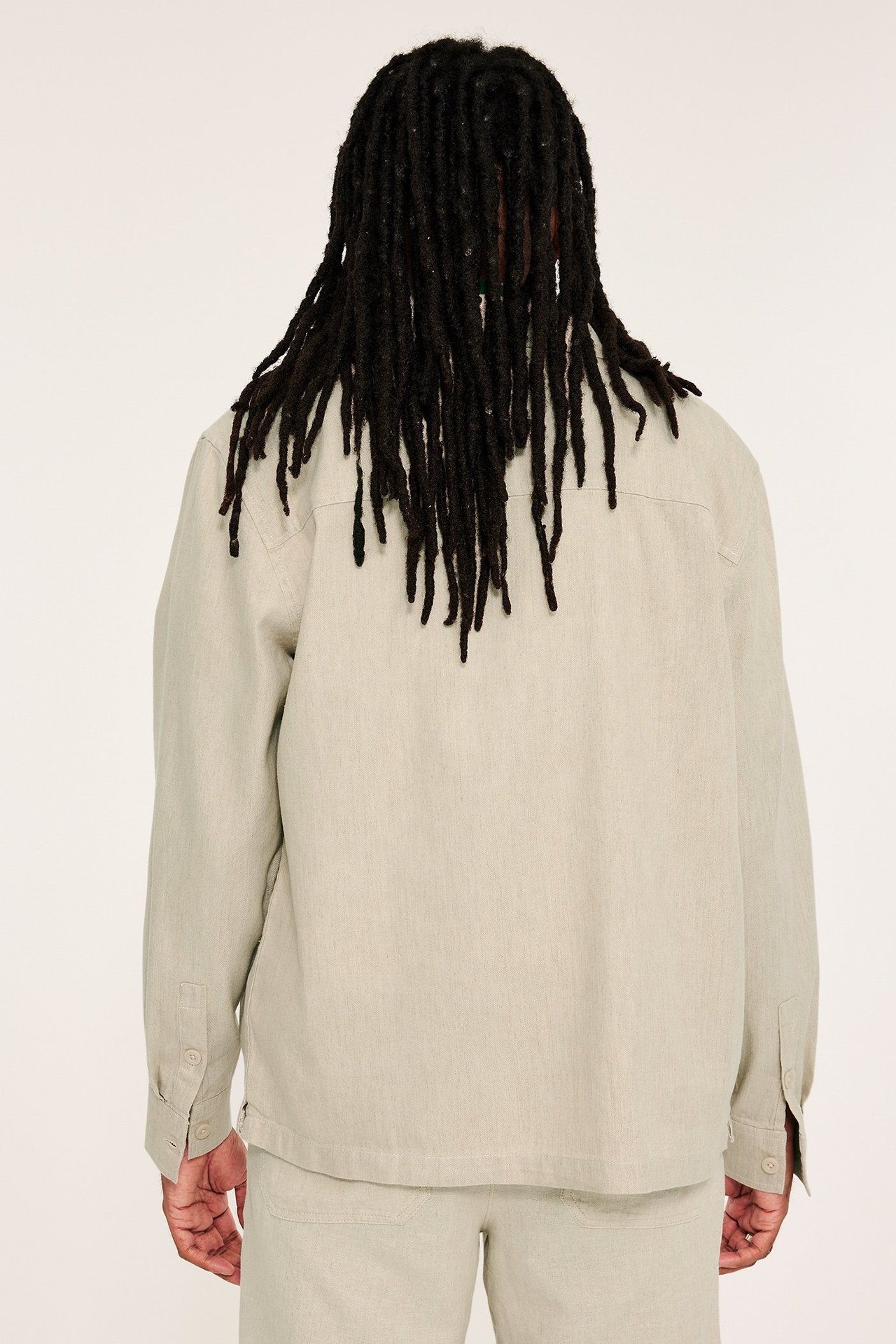 Widok z tyłu mężczyzny w luźnej beżowej lnianej koszuli wierzchniej i pasujących spodniach.