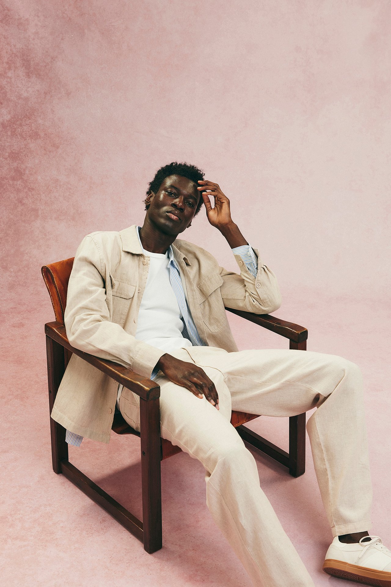 Mies yllään beige pellavasekoitteinen ylipaita, valkoinen t-paita, yhteensopivat housut ja valkoiset tennarit.