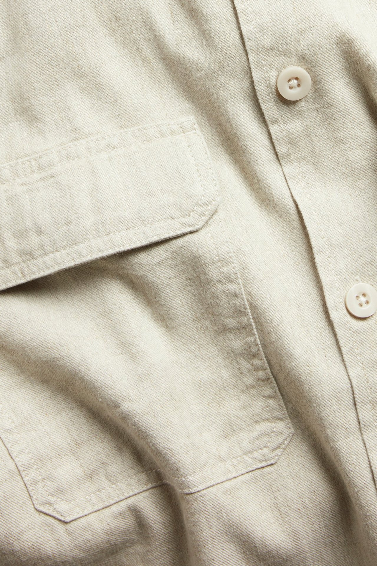 Närbild av en beige linnemix overshirt med två bröstfickor och knappar fram.