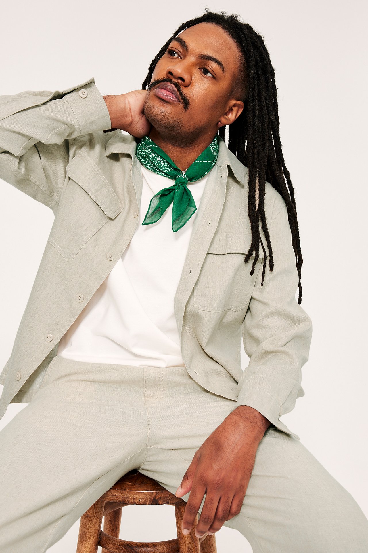 Edestäpäin: mies beige pellavasekoite overshirt, valkoinen t-paita, beiget housut ja vihreä bandana.