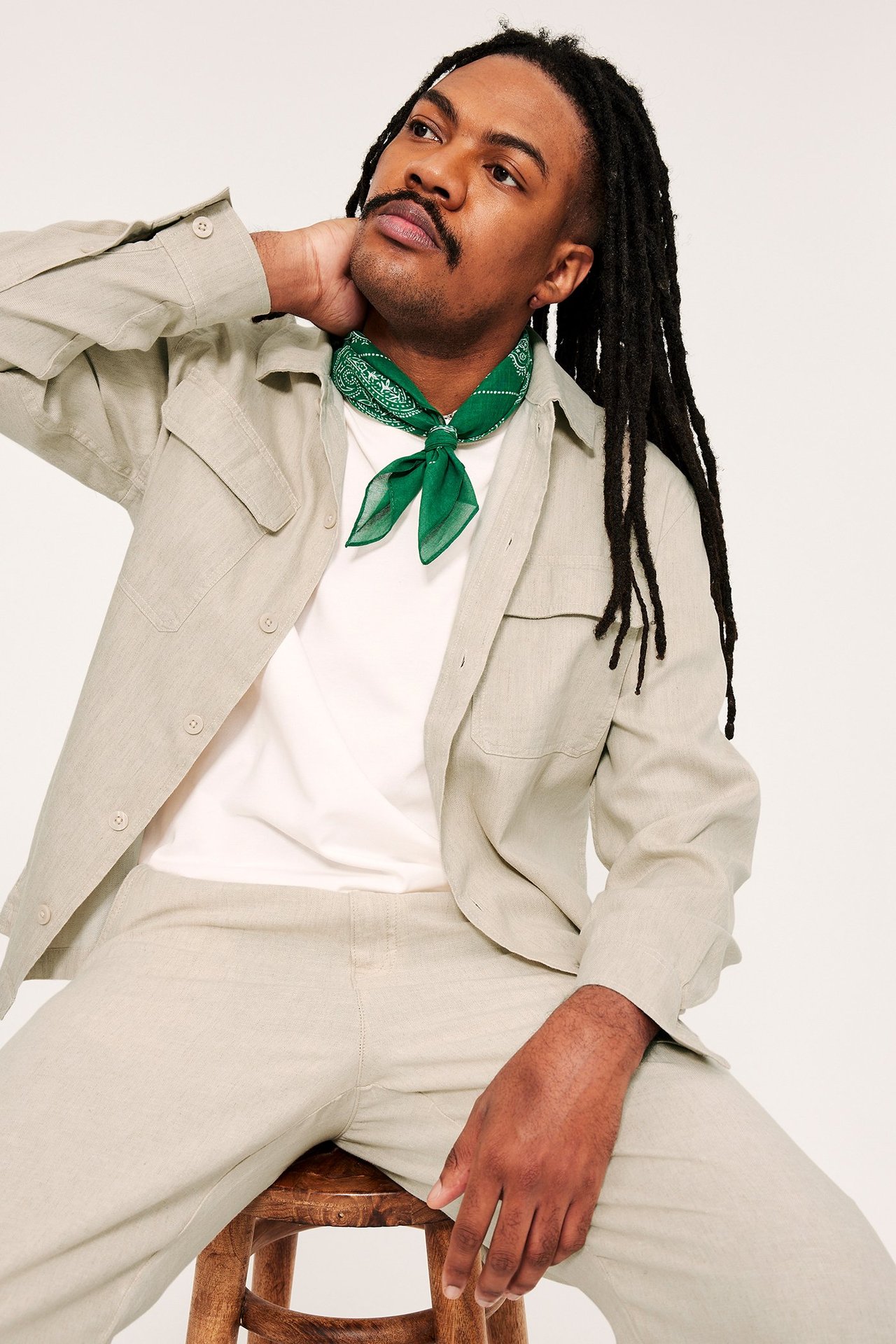 Widok z przodu: mężczyzna w beżowej overshirt z lnu, białym t-shircie, pasujących spodniach i zielonej bandanie.