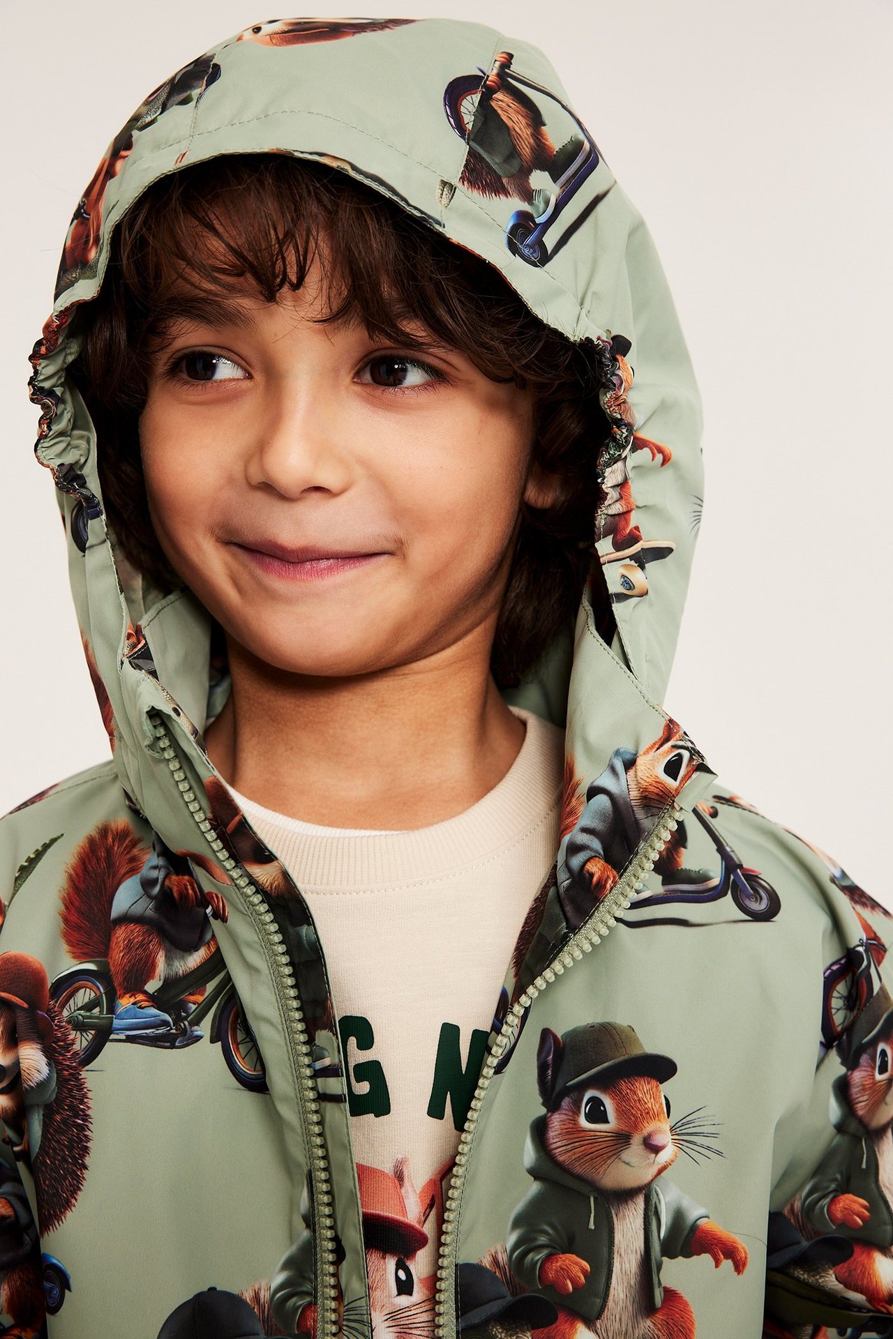 Lähikuva edestä lapsesta, joka käyttää vaaleanvihreää hupullista eläinkuvioista takkia vaalean beigen t-paidan päällä.