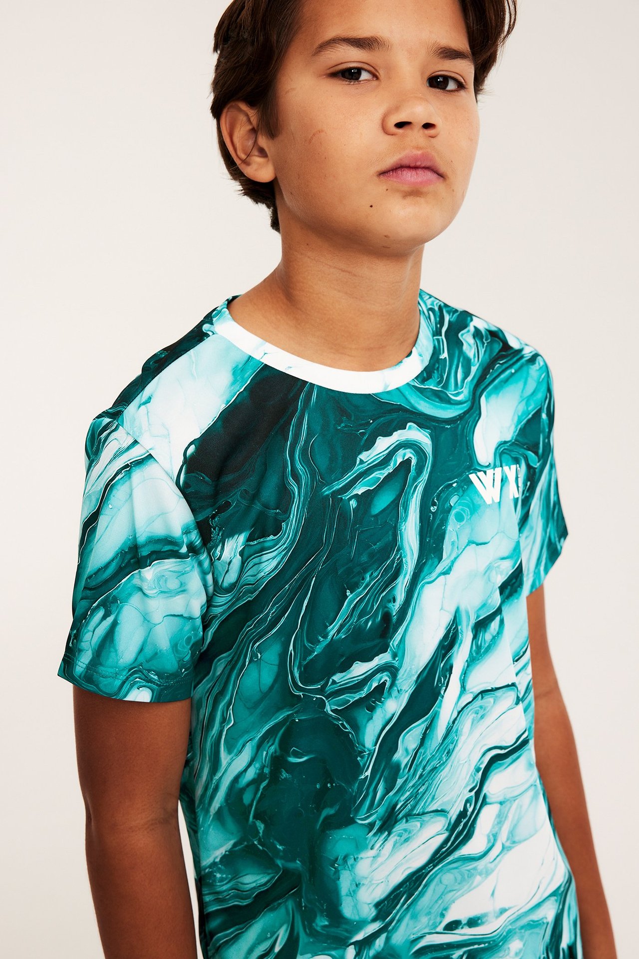 Edestä, lapsi vihreä-valkoisessa kuviollisessa polyesteri-urheilupaidassa, jossa on valkoinen pyöreä pääntie.