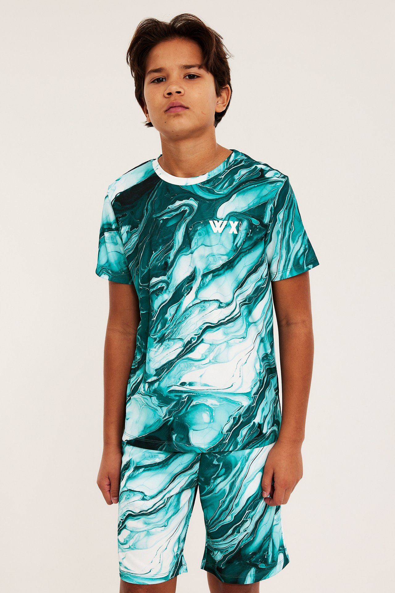 Edestäpäin, poika yllään vihreä-valkoinen marmoroitu polyesteri urheilusetti t-paidan ja shortsien kera.