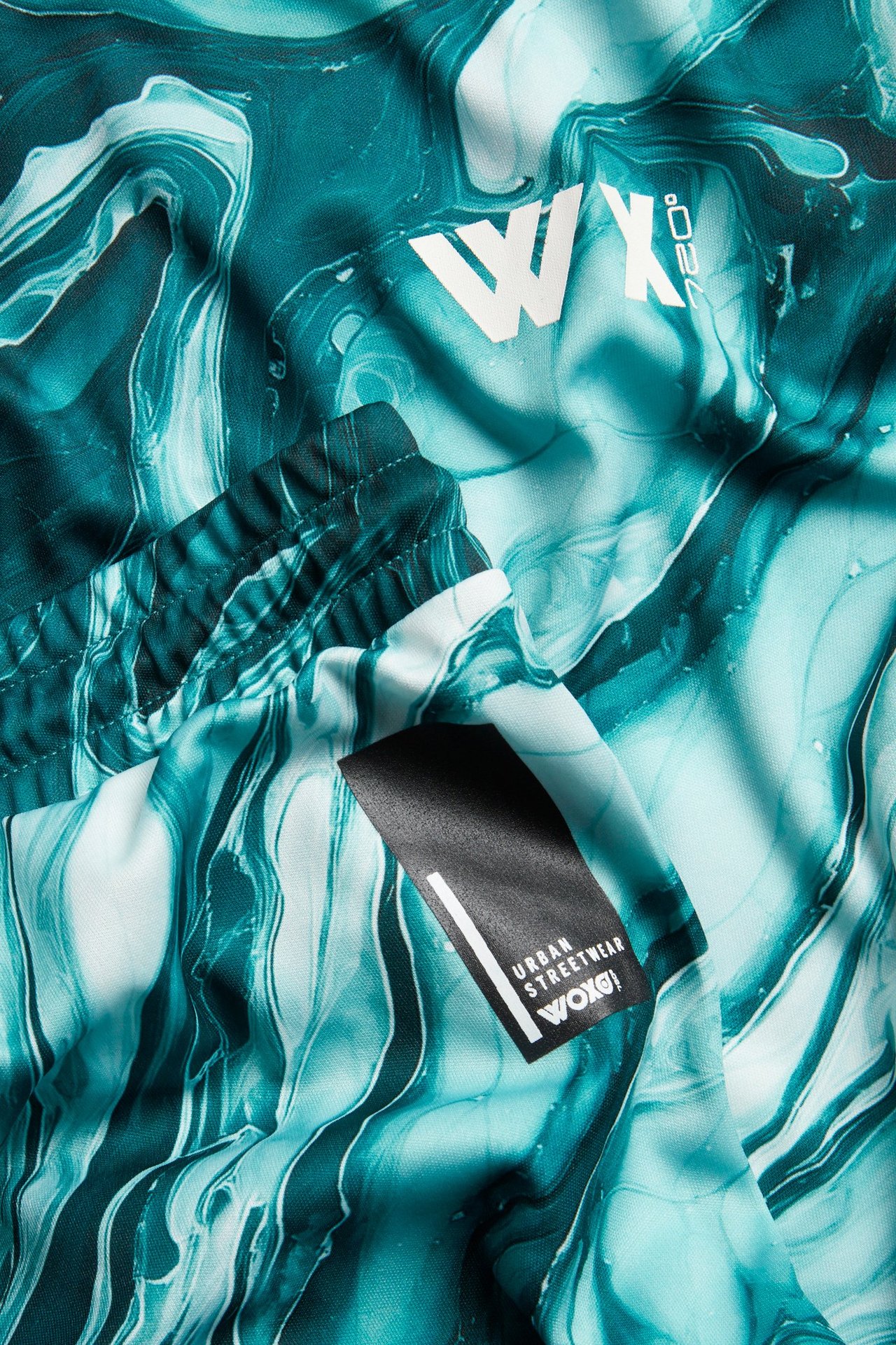 Zbliżenie zielonego, wzorzystego sportowego kompletu z poliestru z marmurkowym nadrukiem i białym logo.