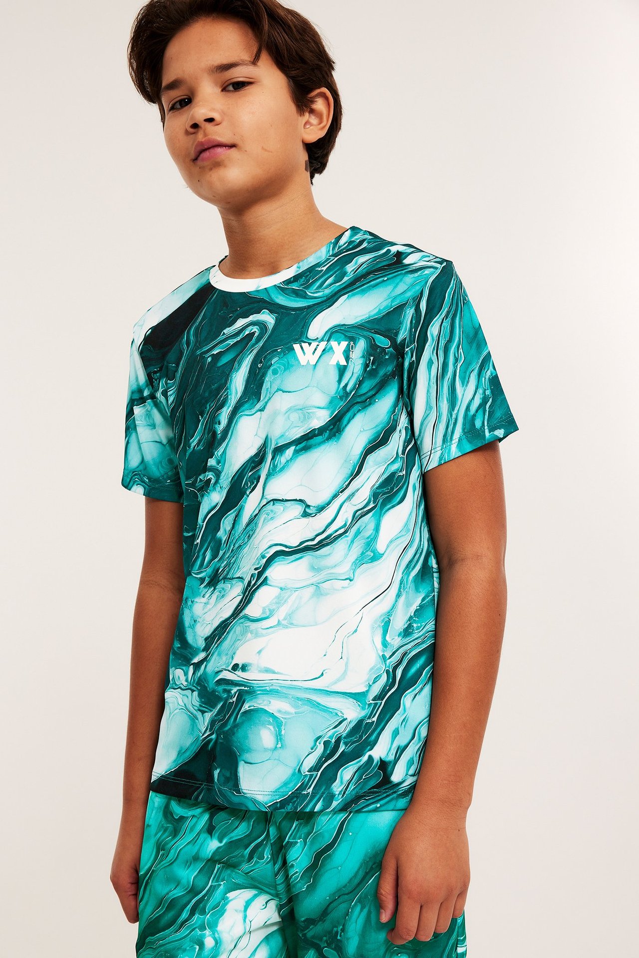 Widok z przodu: dziecko w zielonym, marmurkowym zestawie sportowym z poliestru, z koszulką i szortami.